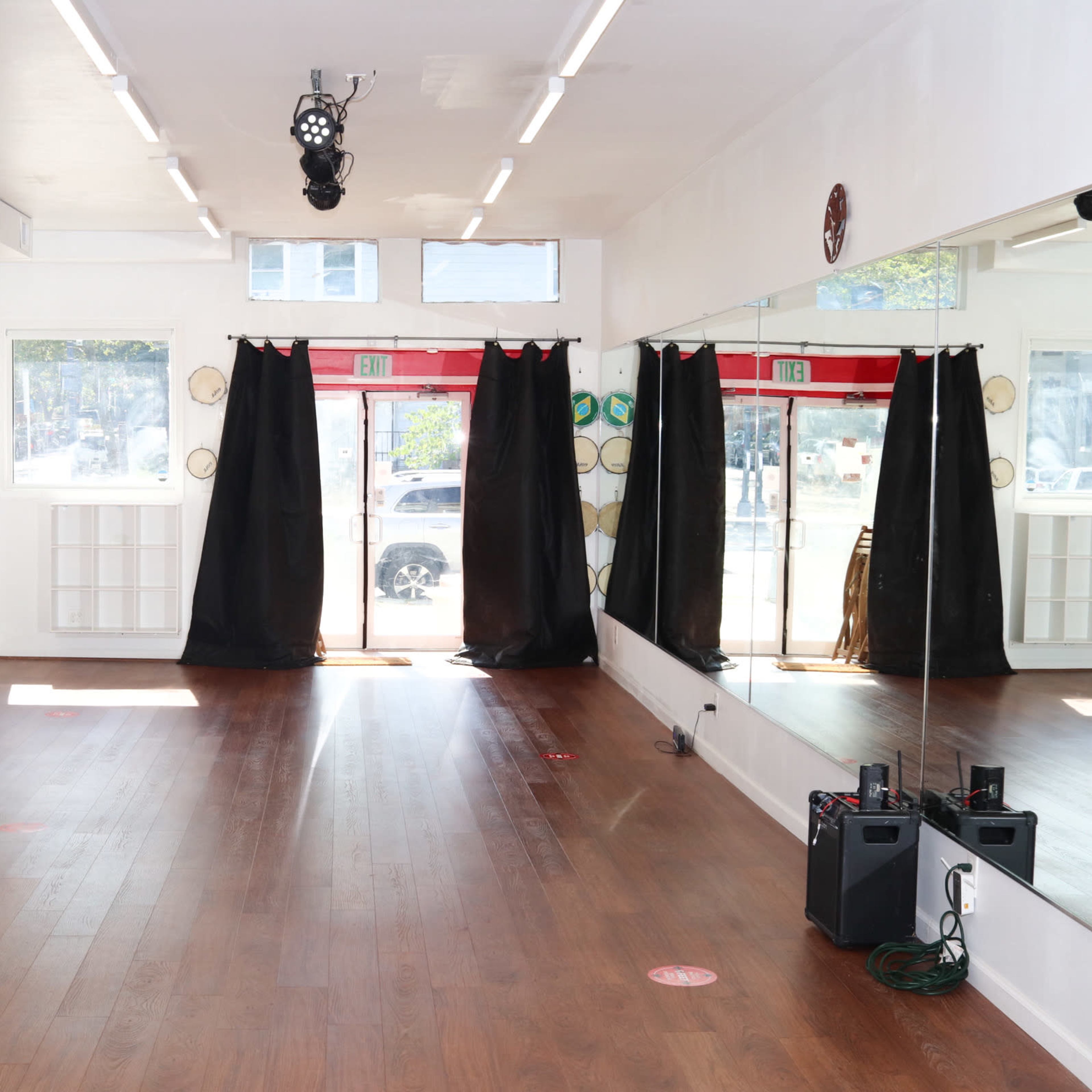 A spacious dance studio with wooden flooring, mirrored walls, and black curtains, adorned with flags and a logo on one wall.
