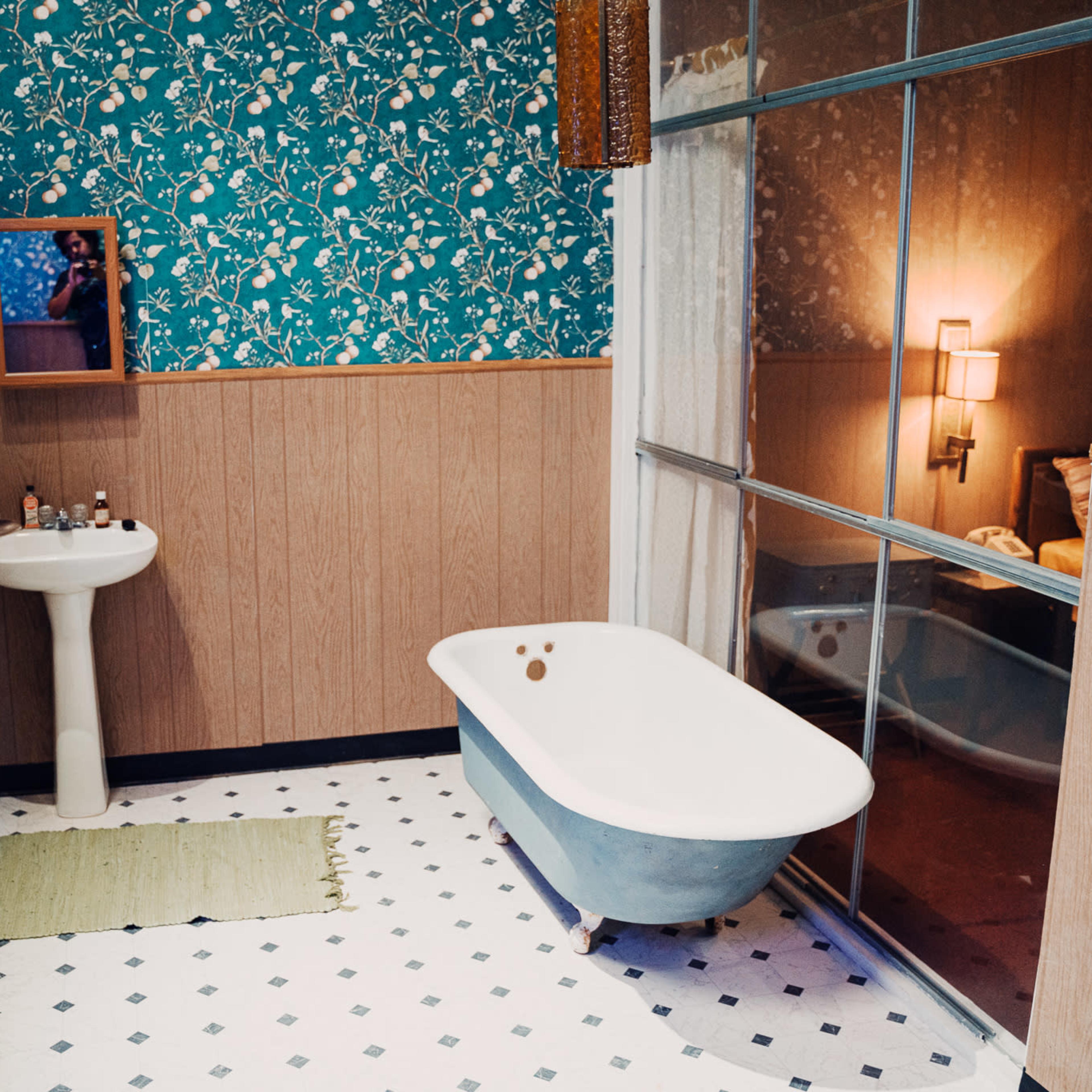 The bathroom features a vintage clawfoot tub, a pedestal sink, and floral wallpaper, with a large window providing natural light.