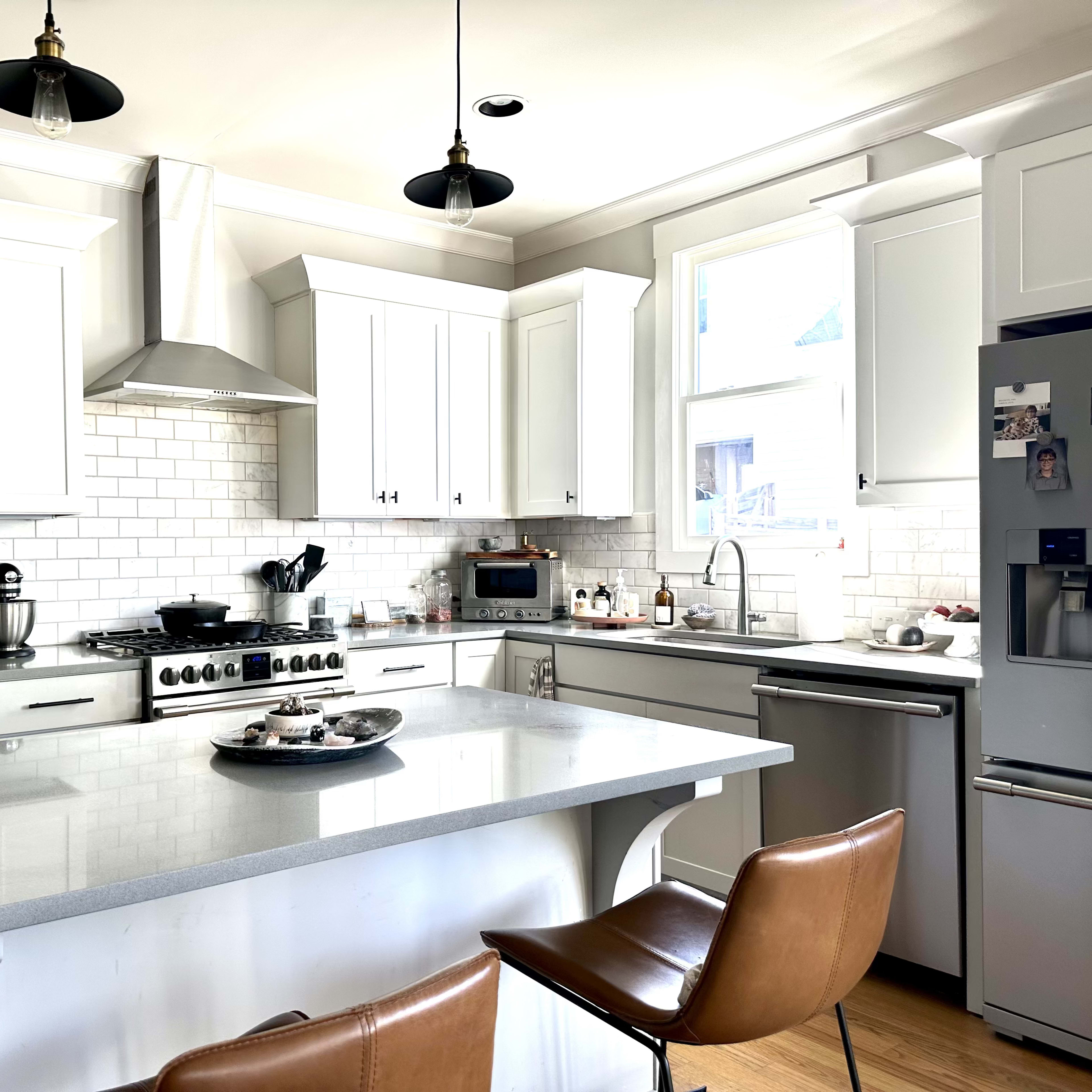 A modern kitchen features white cabinetry, a stainless steel refrigerator, and a large island with leather bar stools.