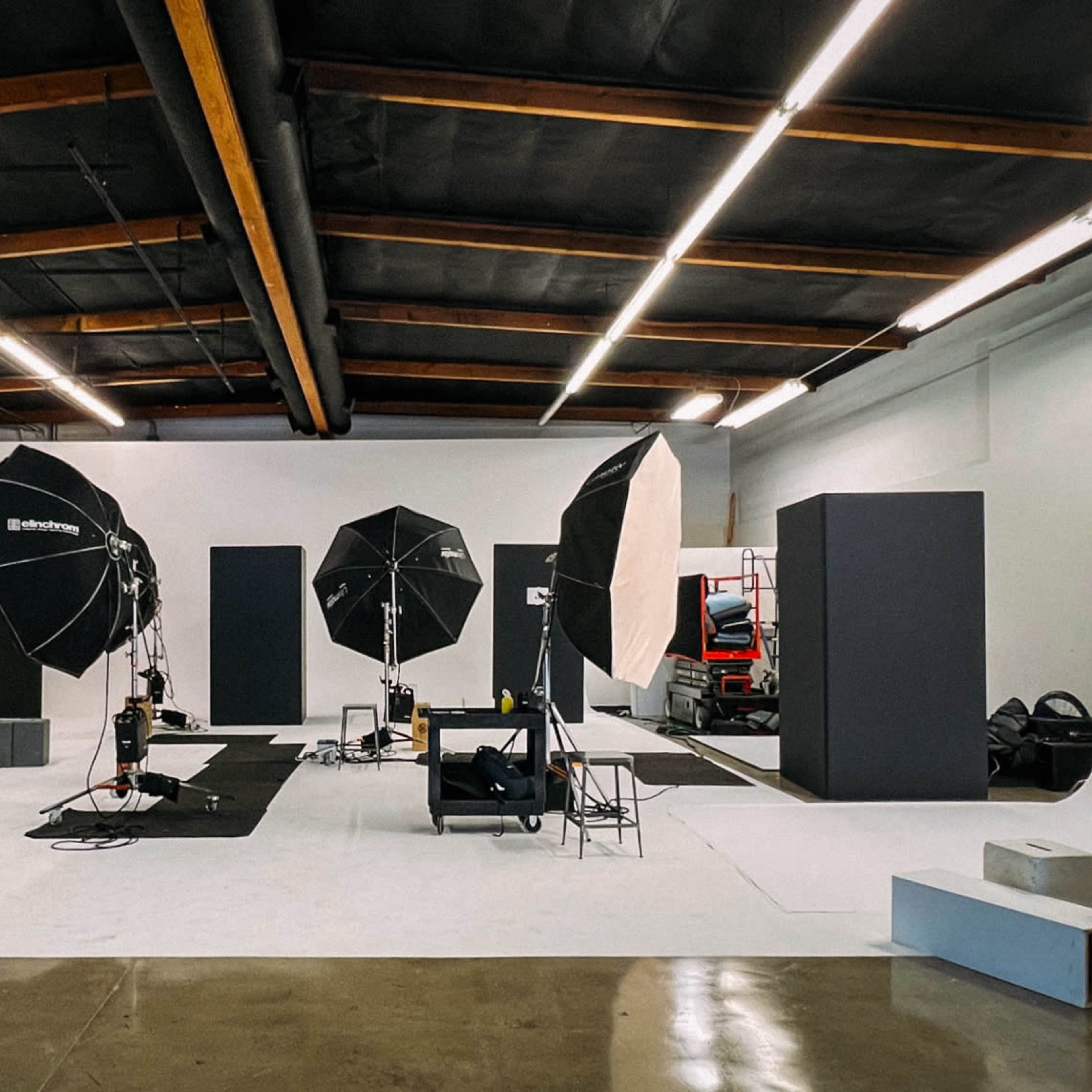 A photography studio is set up with multiple softbox lights, backdrop screens, and a variety of equipment arranged on a white floor.
