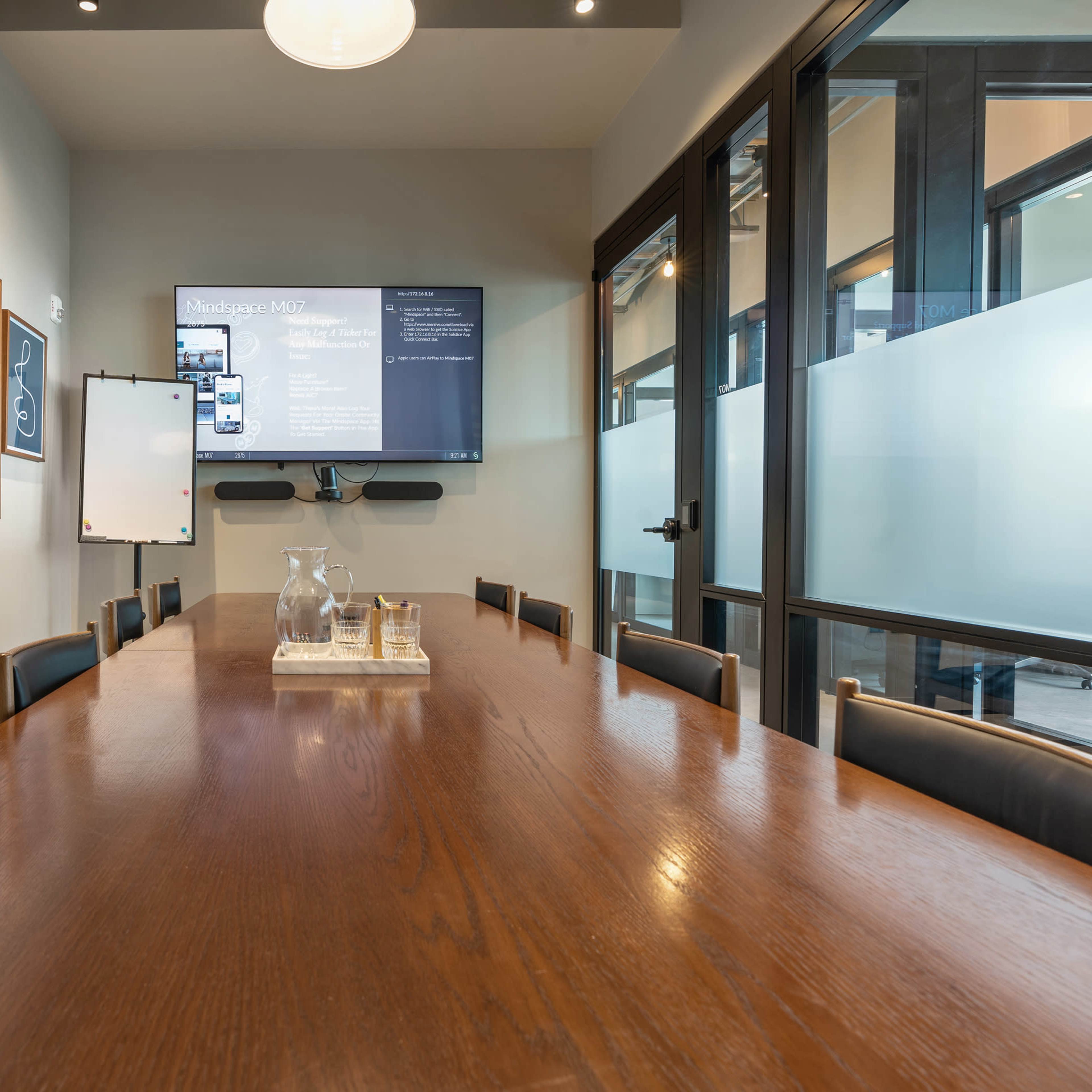 A conference room with a long wooden table, black leather chairs, a television display, and framed art on the walls.