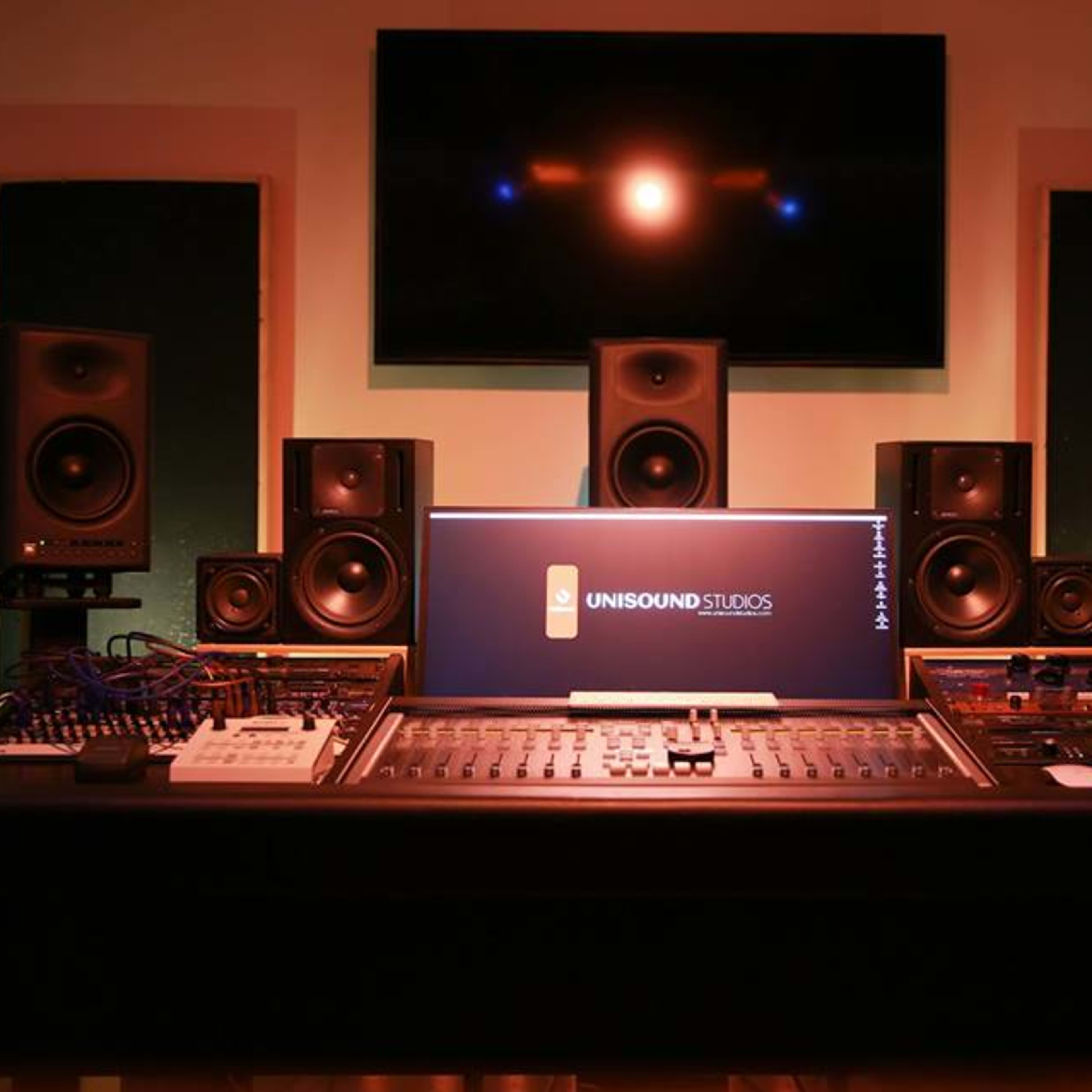 A recording studio setup featuring a large mixing console, studio monitors, and a computer screen displaying the logo "UNISOUND STUDIOS."