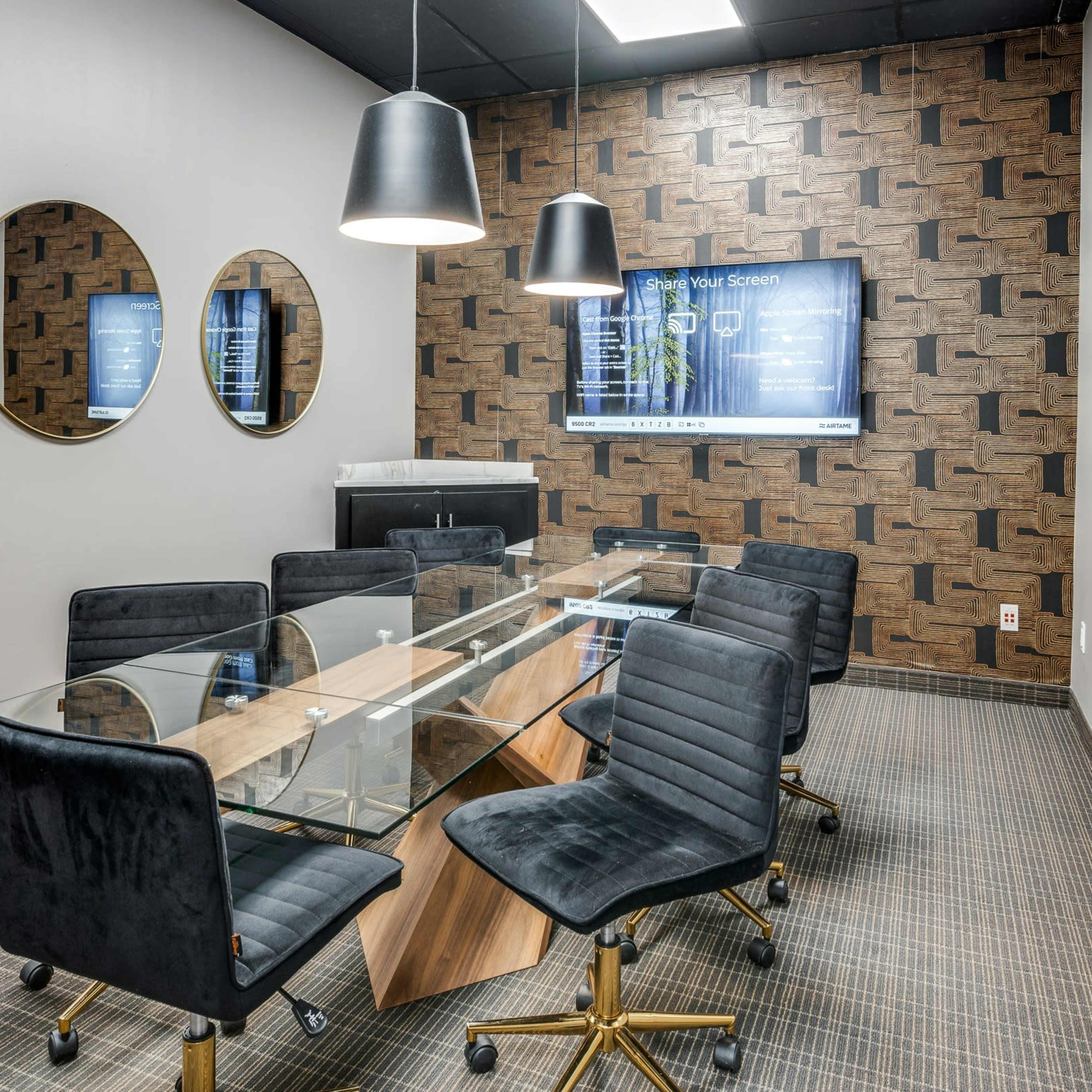 A modern conference room featuring a glass table with six black chairs, three round mirrors on the walls, and a large screen displaying information.