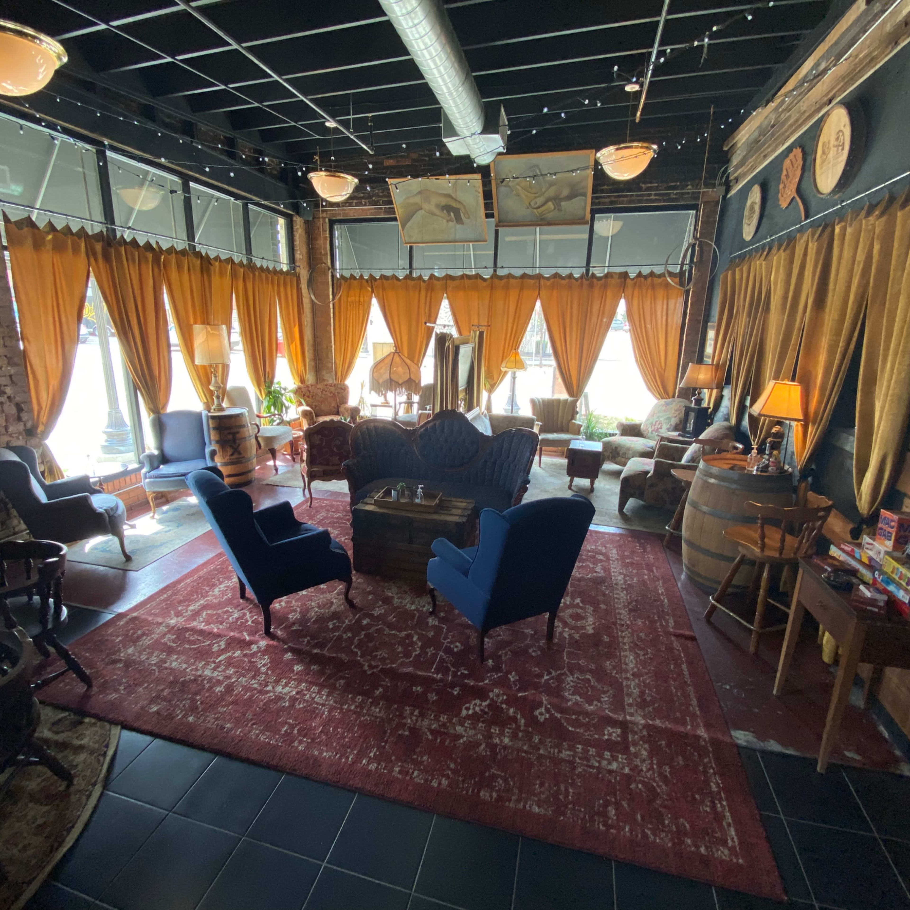 A cozy lounge area with plush blue chairs, wooden furniture, and large windows draped with orange curtains.