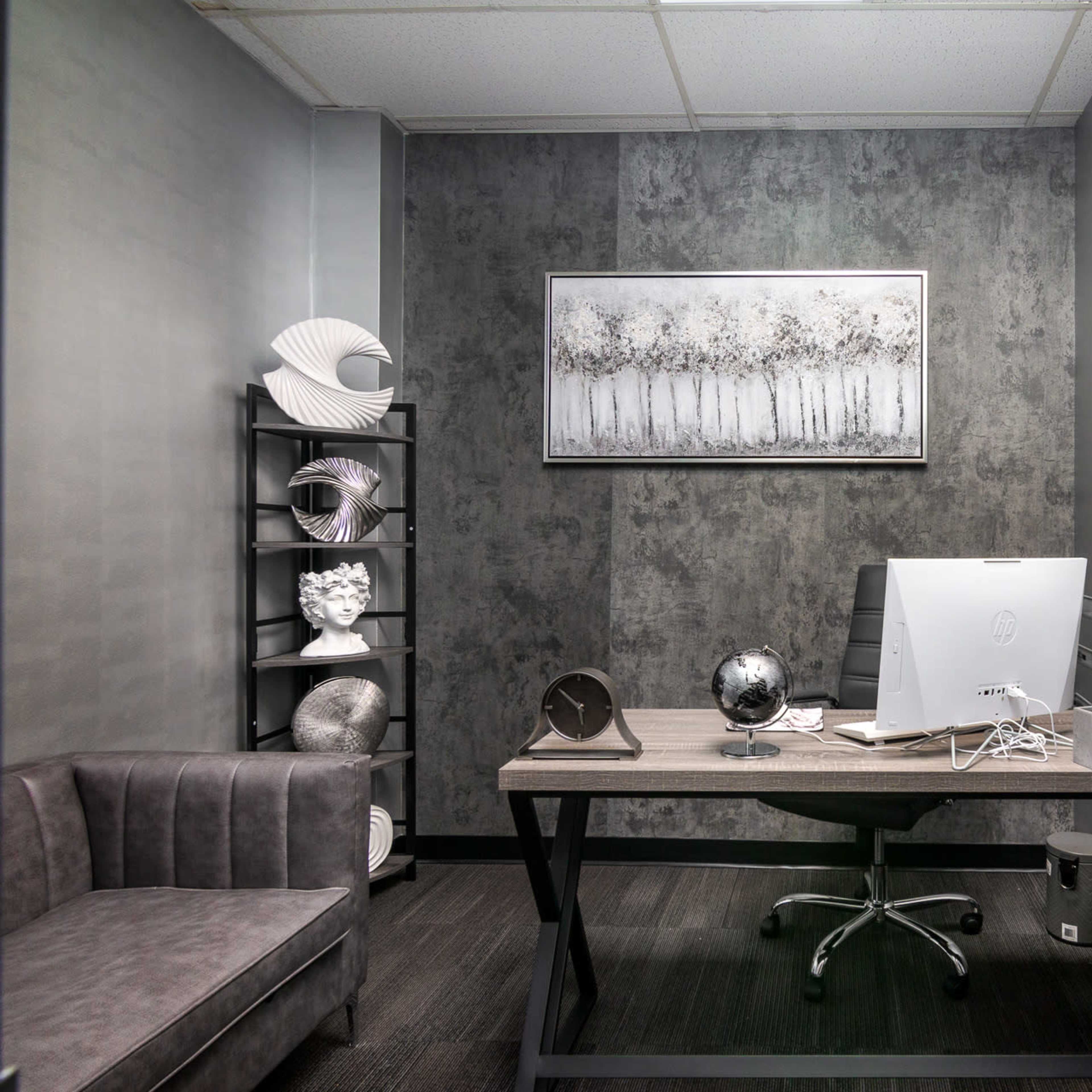 A modern office space features a desk with a computer, decorative sculptures, and a chair, set against a textured wall and framed artwork.