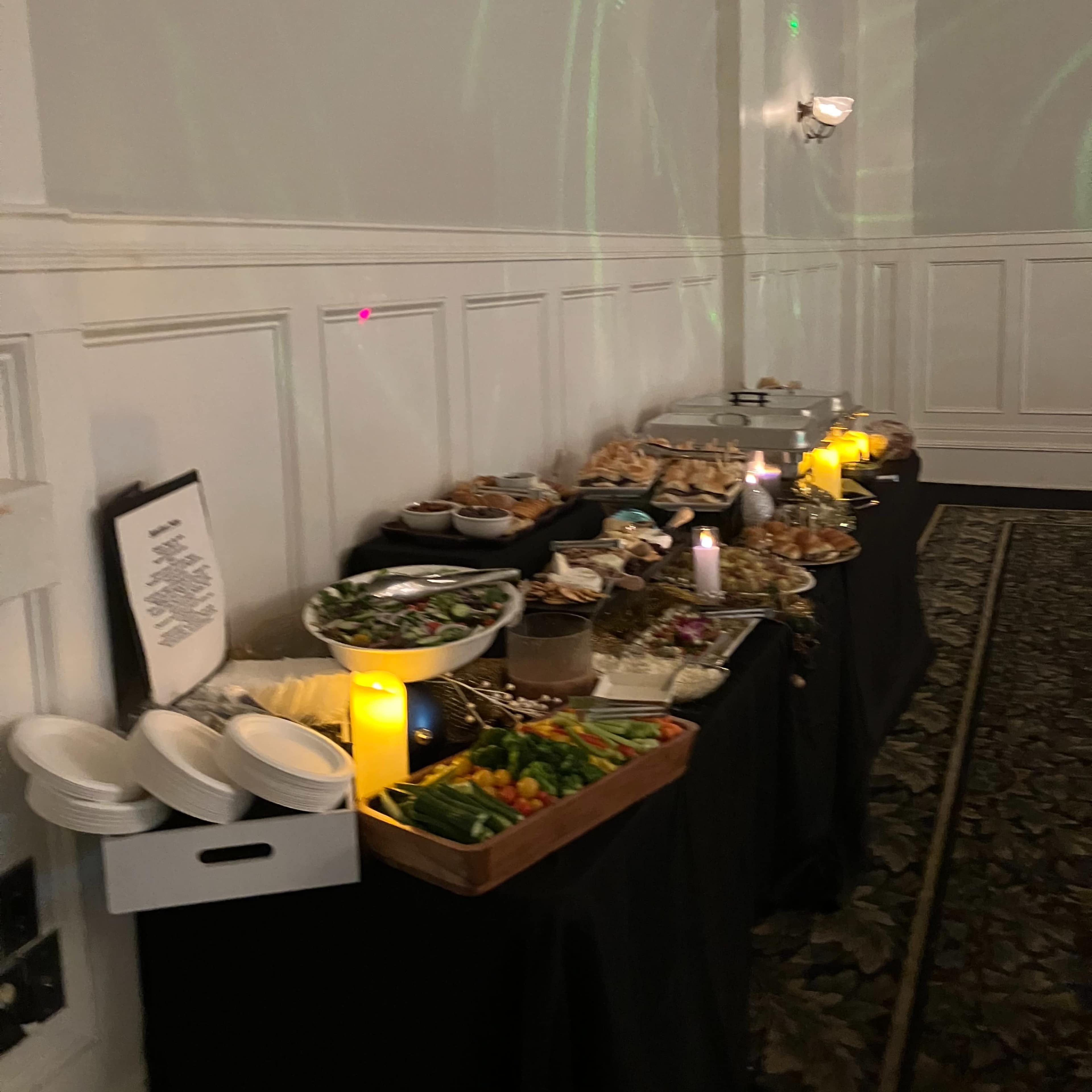 A buffet table is set up with various dishes, snacks, and decorative candles in a banquet hall.