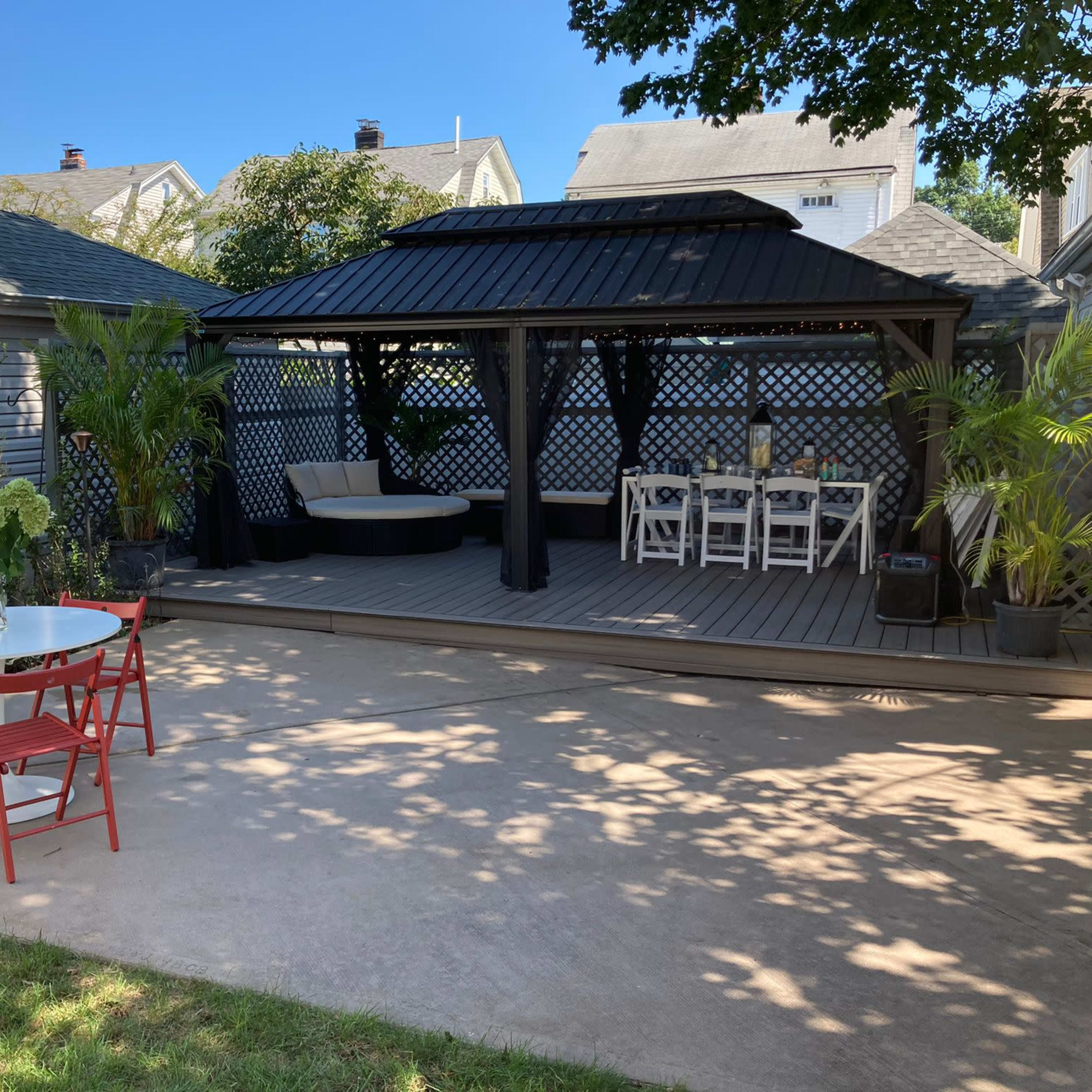 A landscaped backyard with a pergola, dining area, red chairs, and a hammock amidst surrounding greenery.