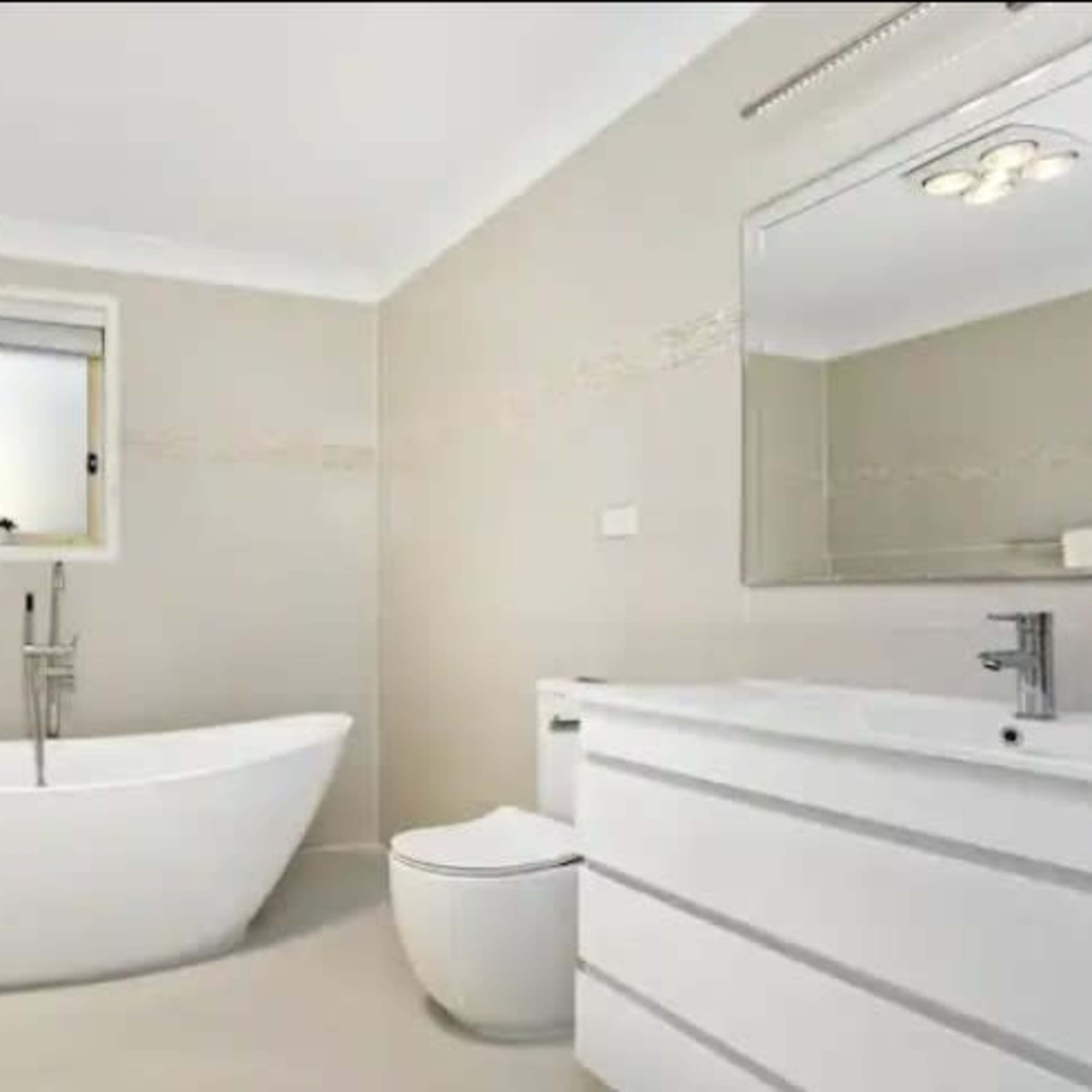 A modern bathroom featuring a freestanding bathtub, a wall-mounted sink with a storage cabinet, and a toilet.