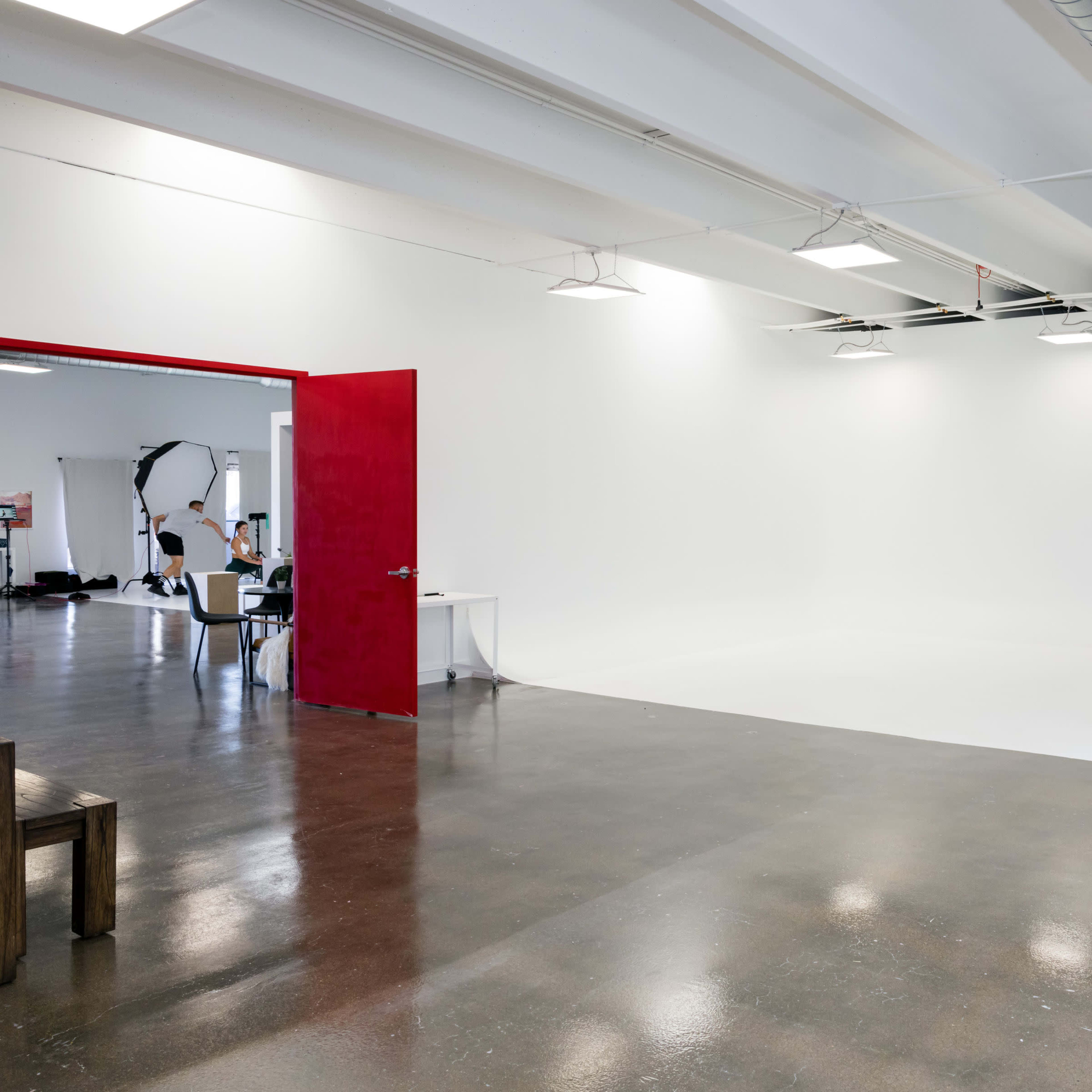 A spacious, minimalist studio with a bright white backdrop and a red door leading to another area.