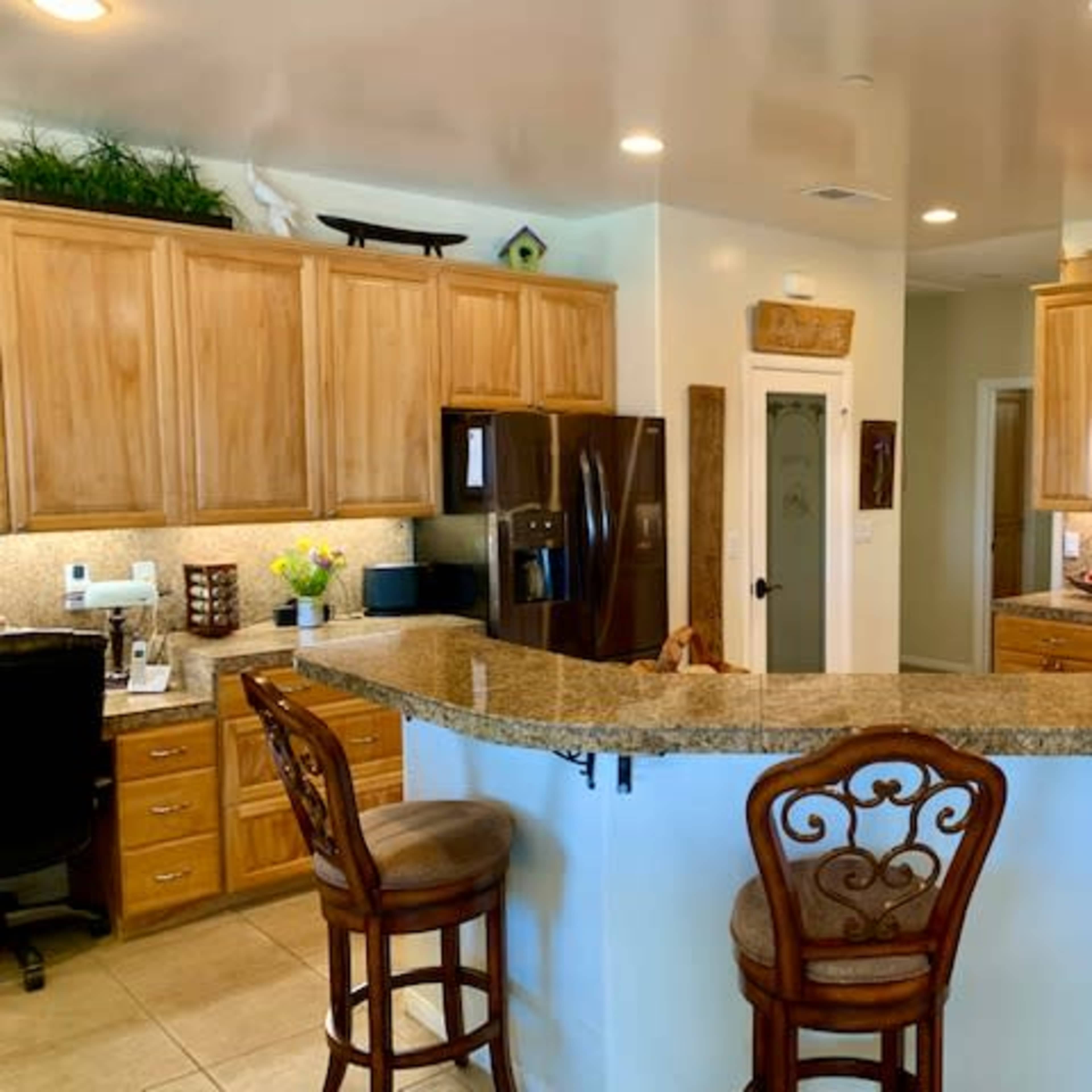 A modern kitchen featuring wooden cabinets, a granite countertop with bar seating, and stainless steel appliances.