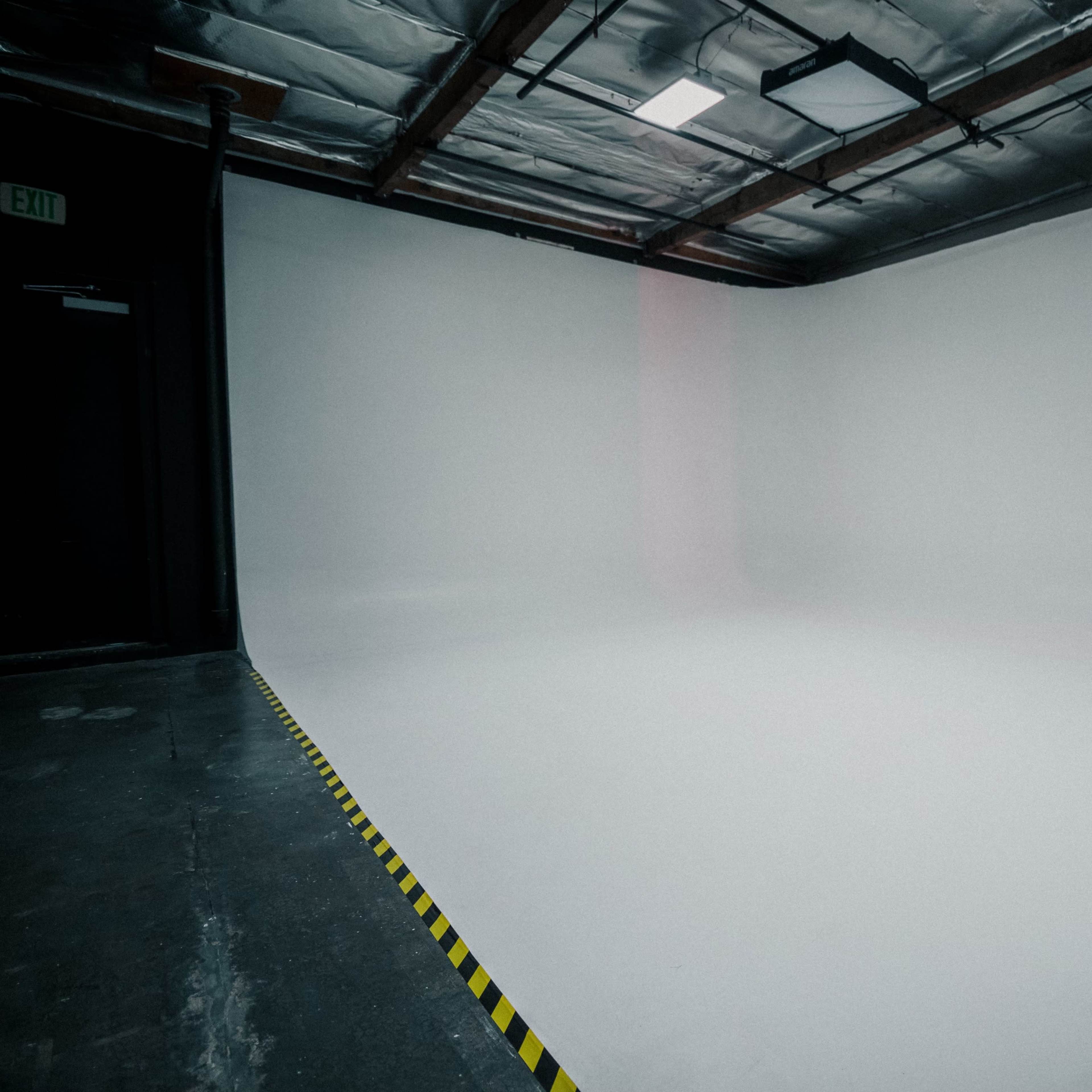 A spacious, empty studio with a smooth white background and yellow caution tape along the floor.