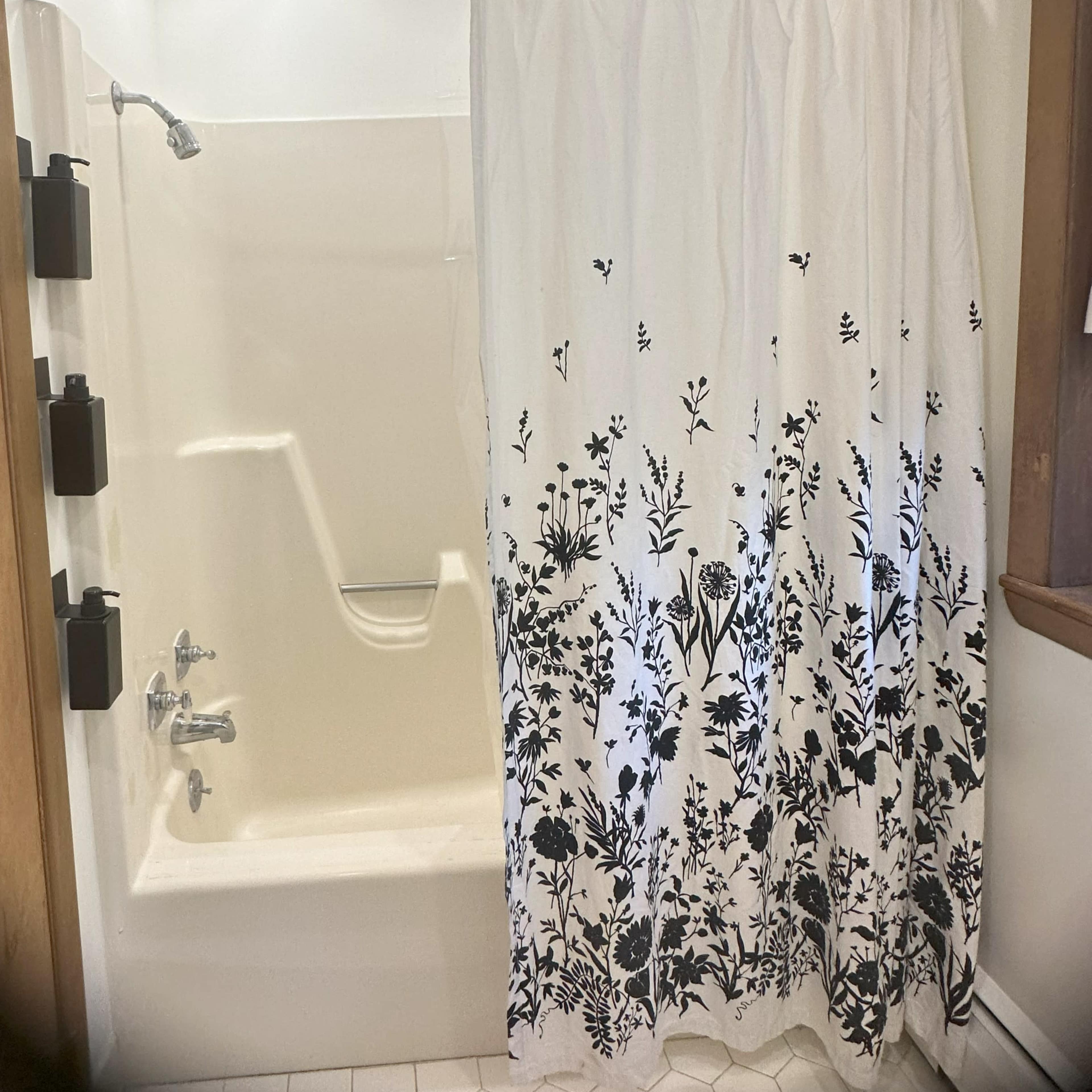 A bathroom scene with a shower, curtain, and white bathtub.