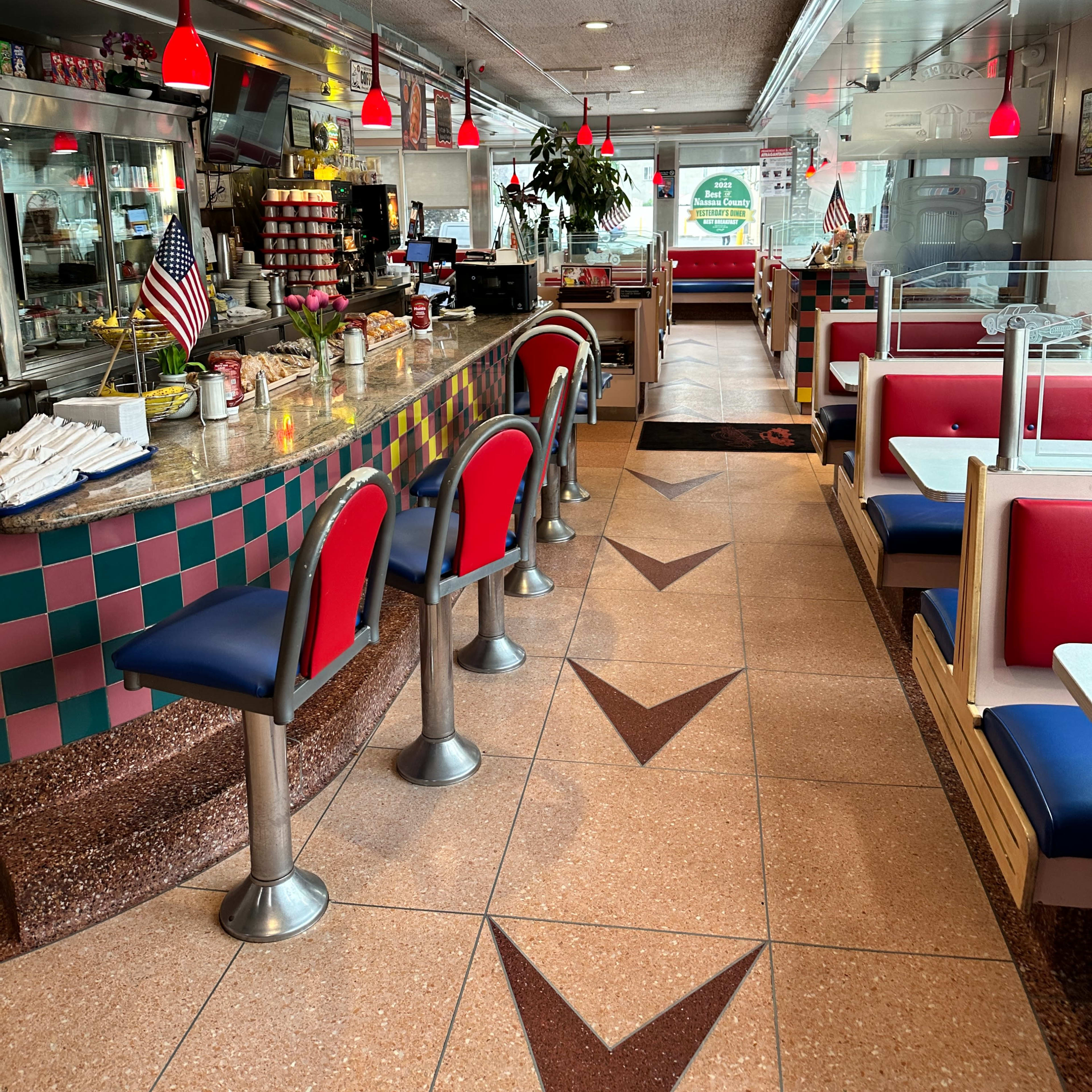 The interior of a diner with a long counter, bar stools, and booths lined along the walls, featuring red and blue seating.