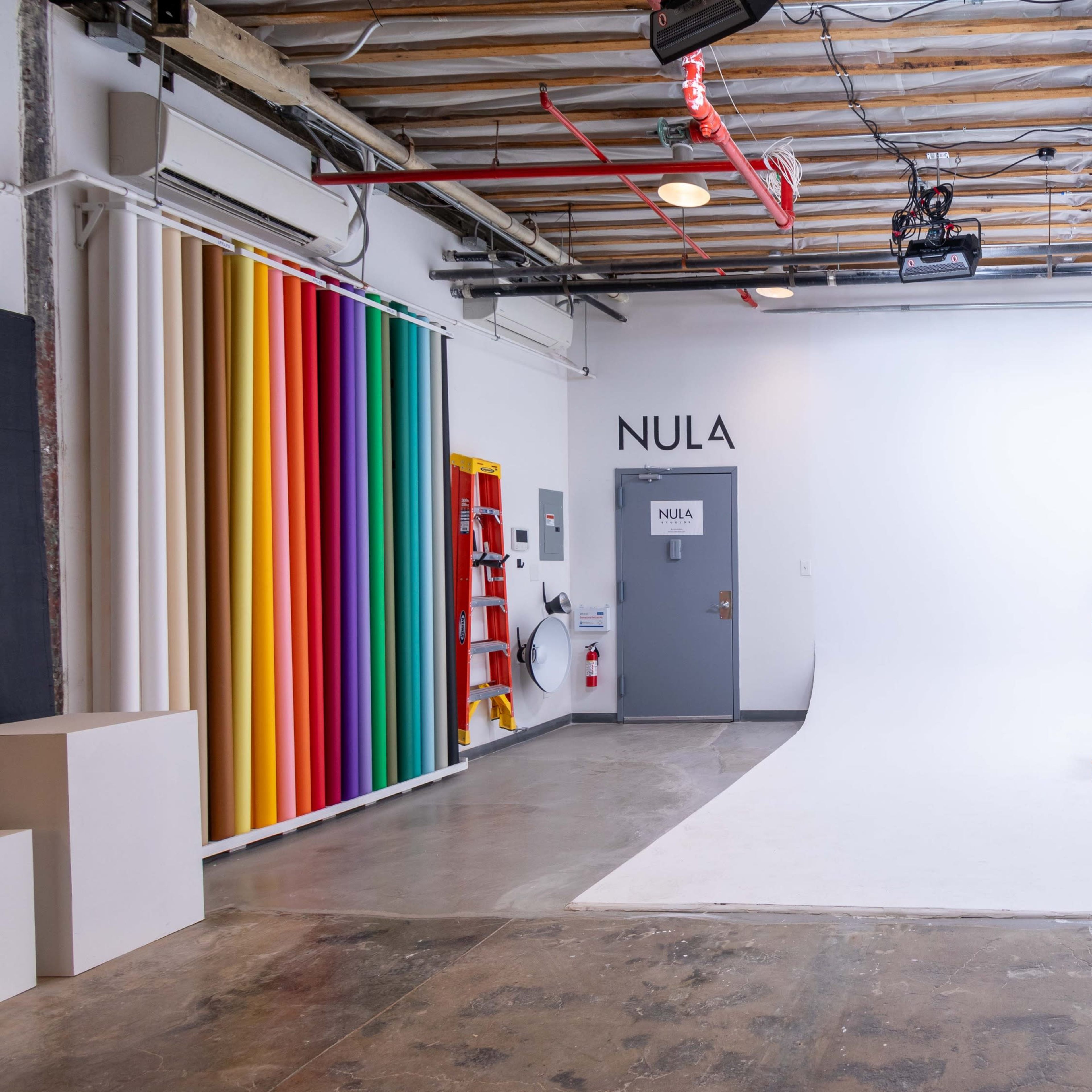 A minimalist photo studio with a white backdrop, a wooden director's chair in the center, and colorful striped panels on the side walls.