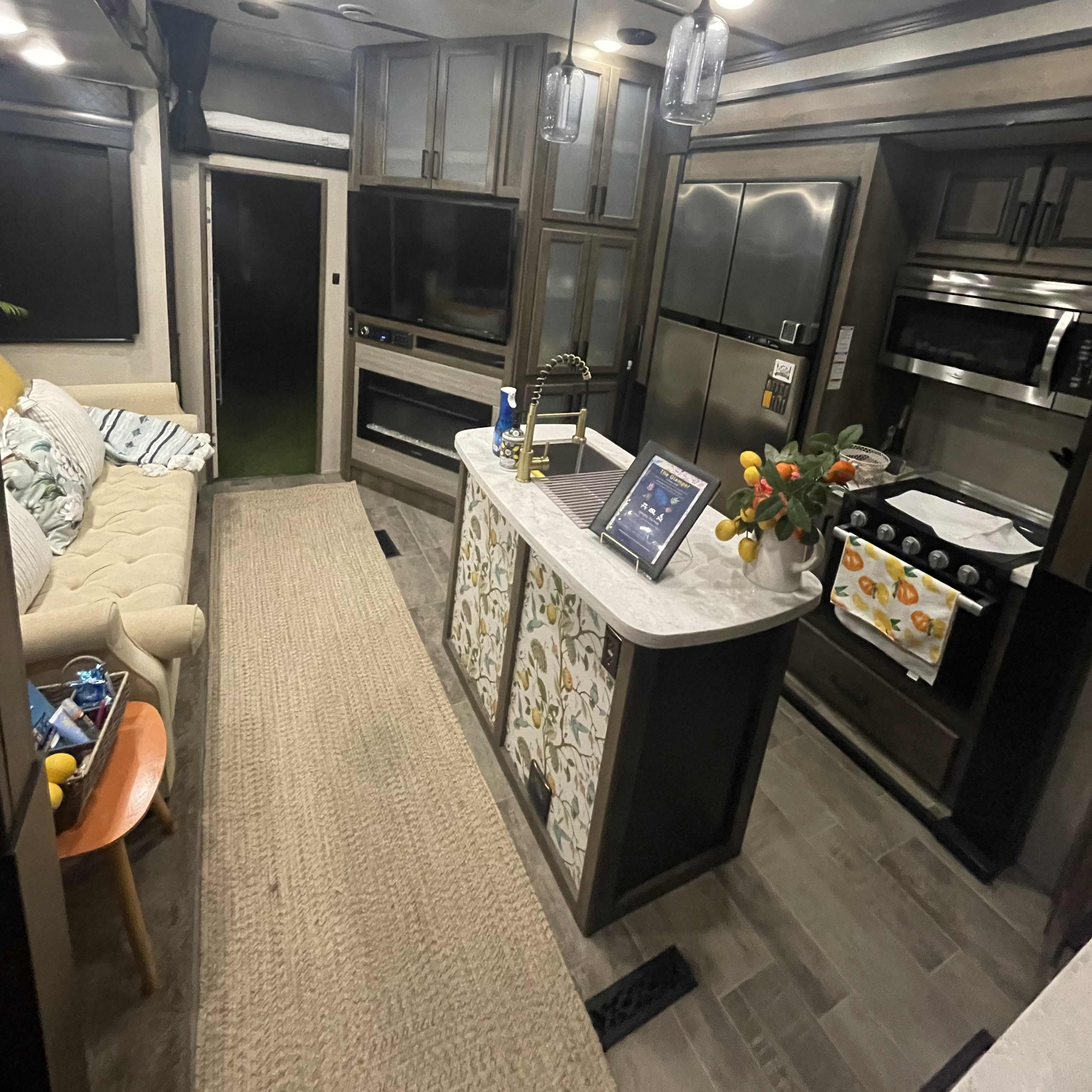 The interior of a modern RV with a cozy seating area, a kitchen island with decorative elements, and various appliances along the walls.