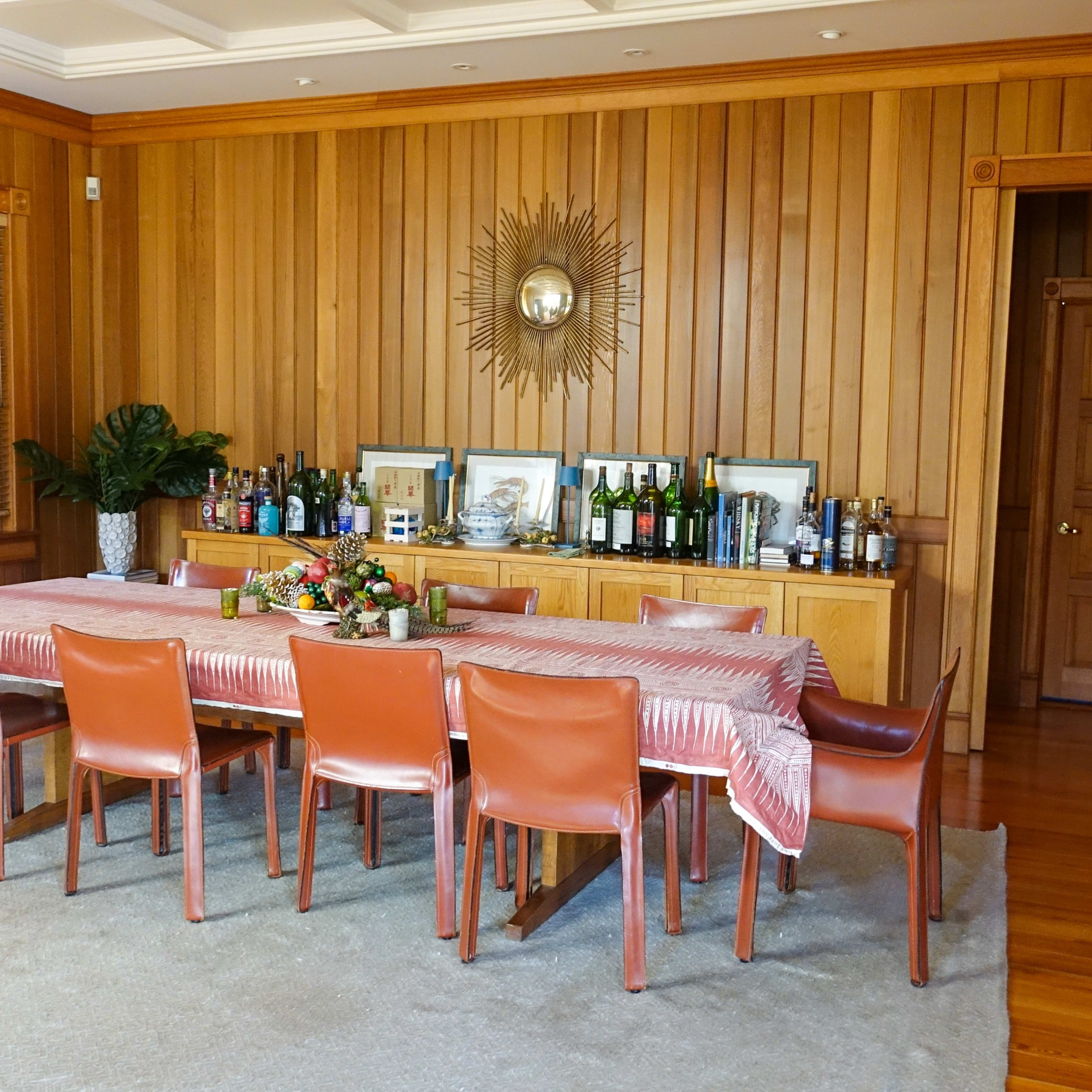A wooden-paneled dining room with a long table set for a meal and a sideboard displaying various bottles and framed pictures.