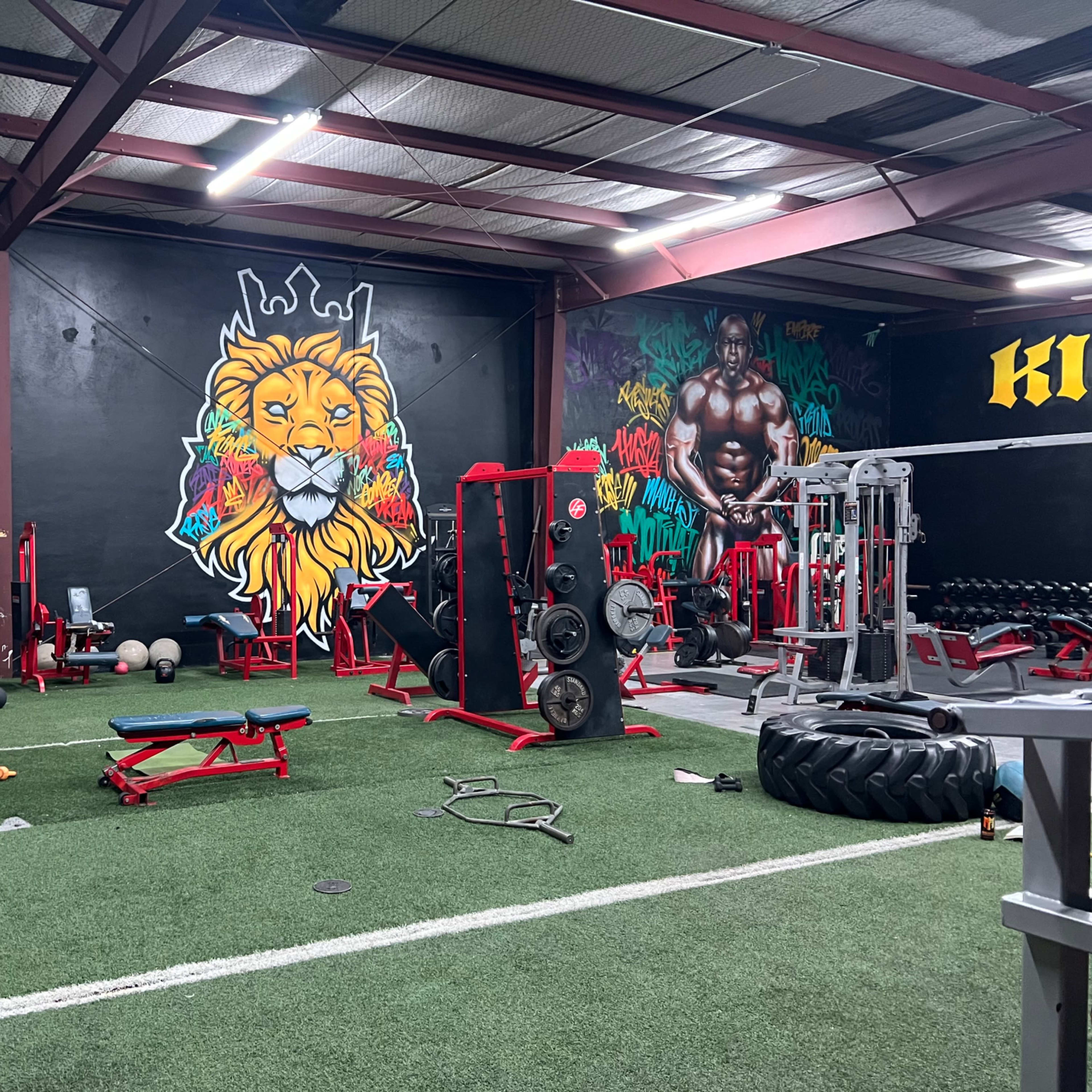 A gym with various workout equipment and colorful murals on the walls featuring a lion and a muscular figure.