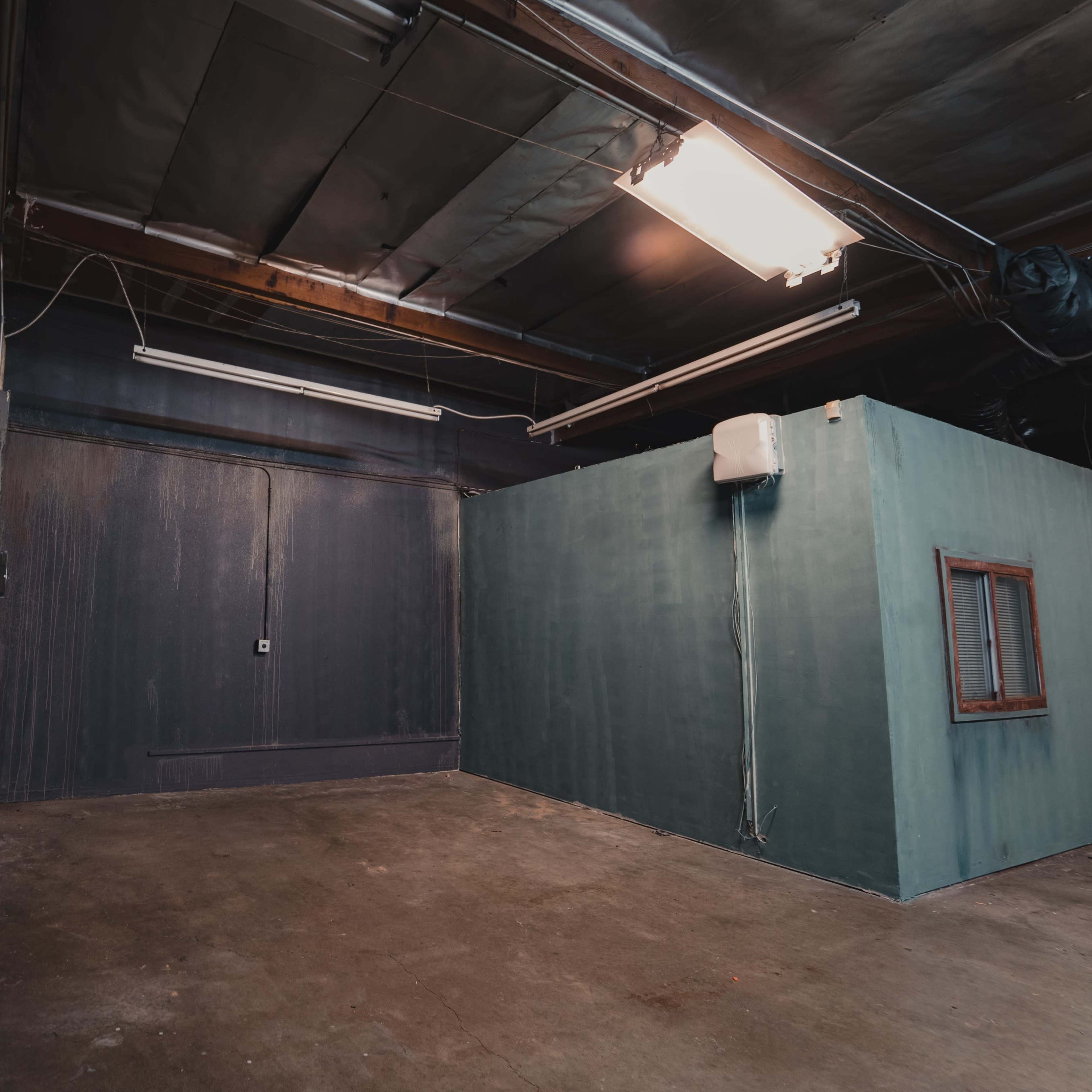 An industrial room with one dark wall, a blue-green wall with a small window, and a door on the left side.