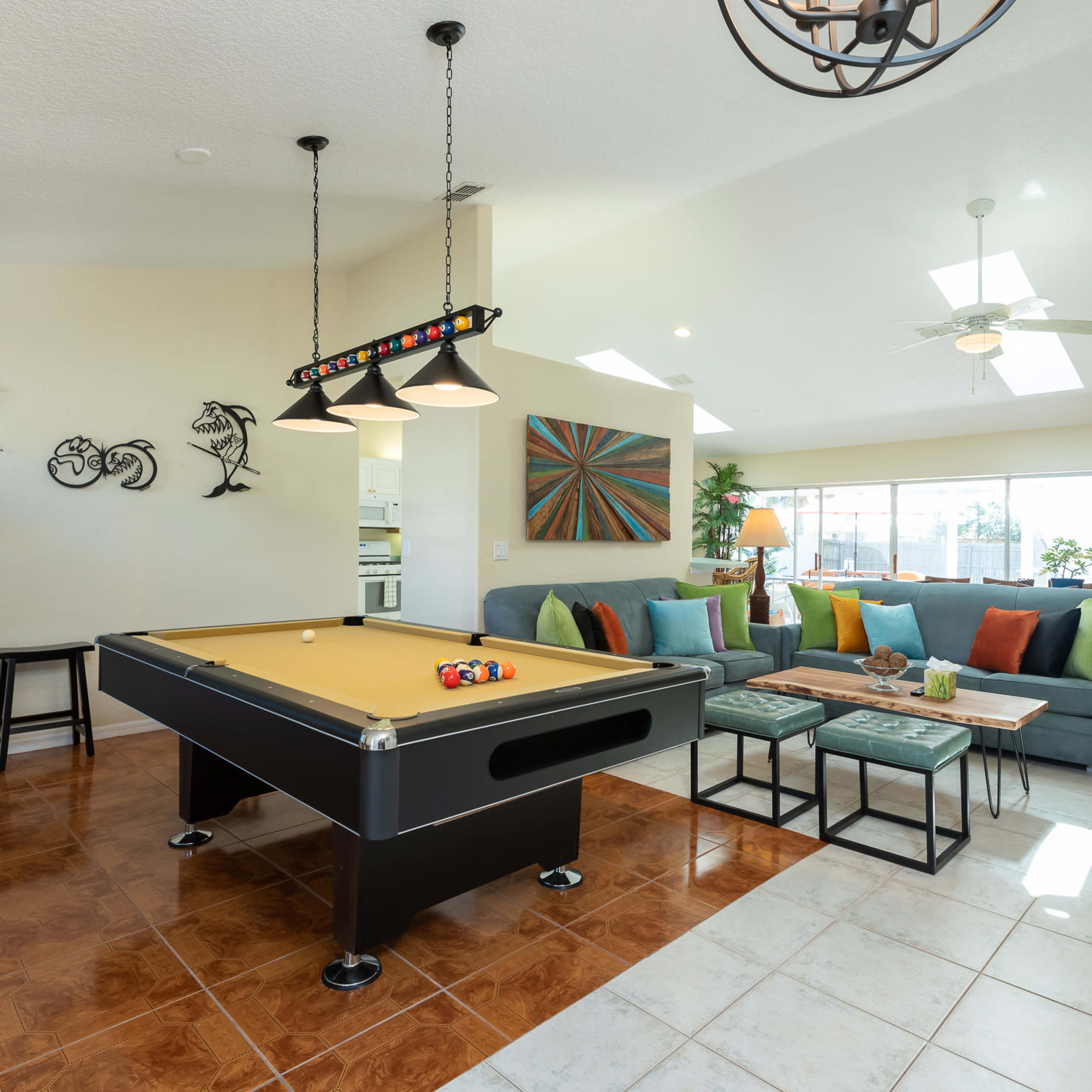 A spacious living area featuring a billiard table, a large sectional sofa with colorful cushions, and various decorative elements on the walls.