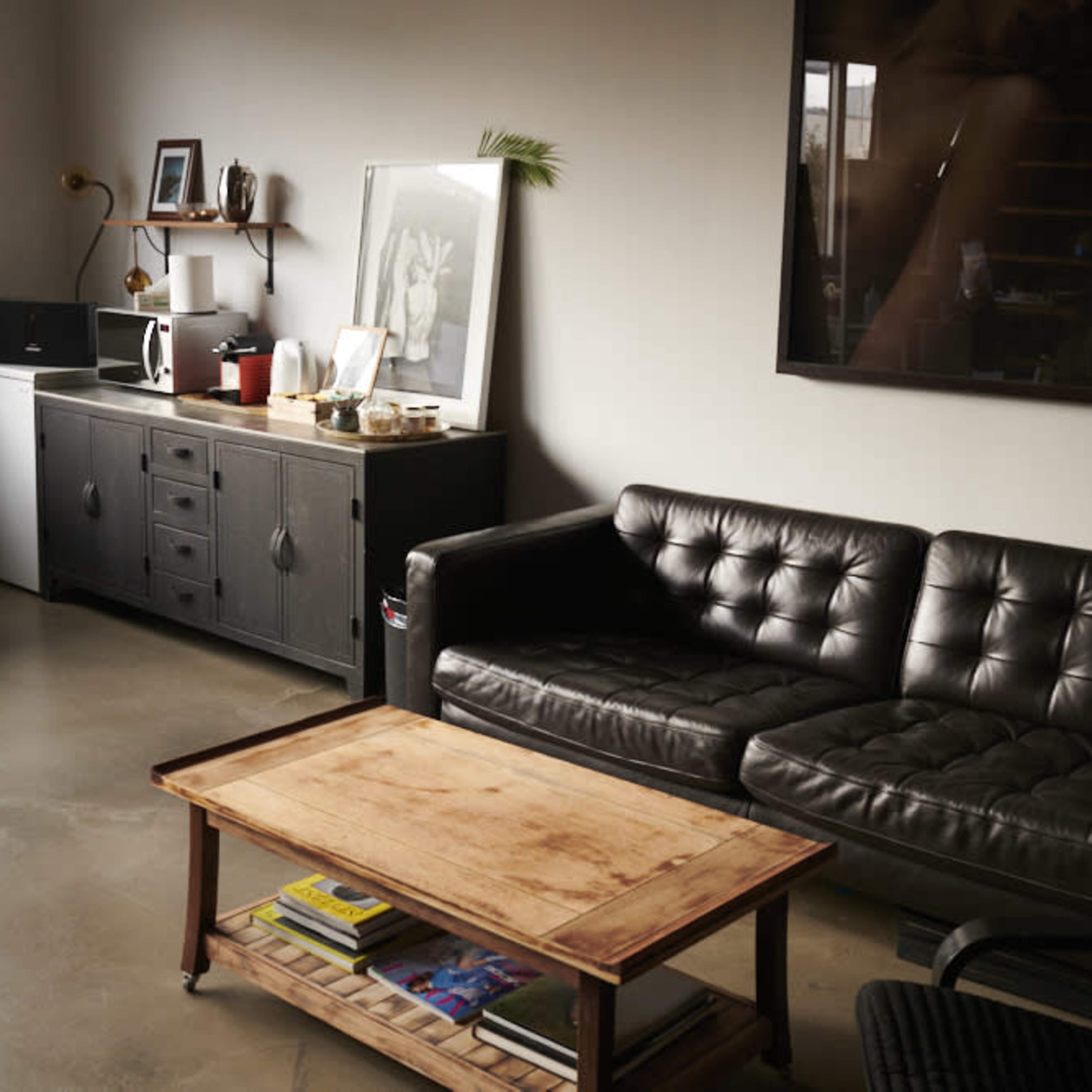A modern living room with a black leather sofa, a wooden coffee table, a sideboard, and various decorative items on the walls and surfaces.