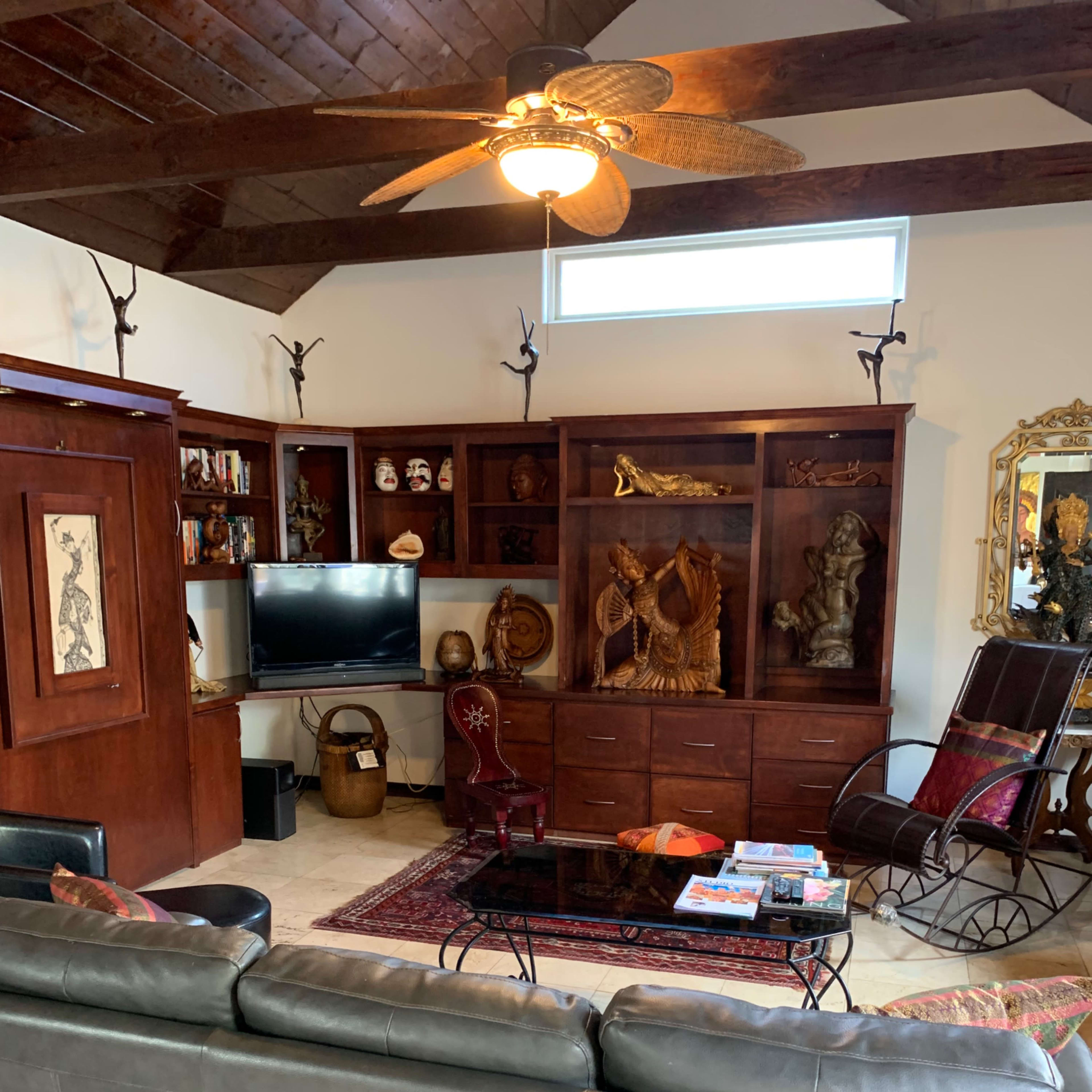 A living room with wooden shelves displaying various decorative items, a television, and a gray sofa facing a coffee table on a rug.