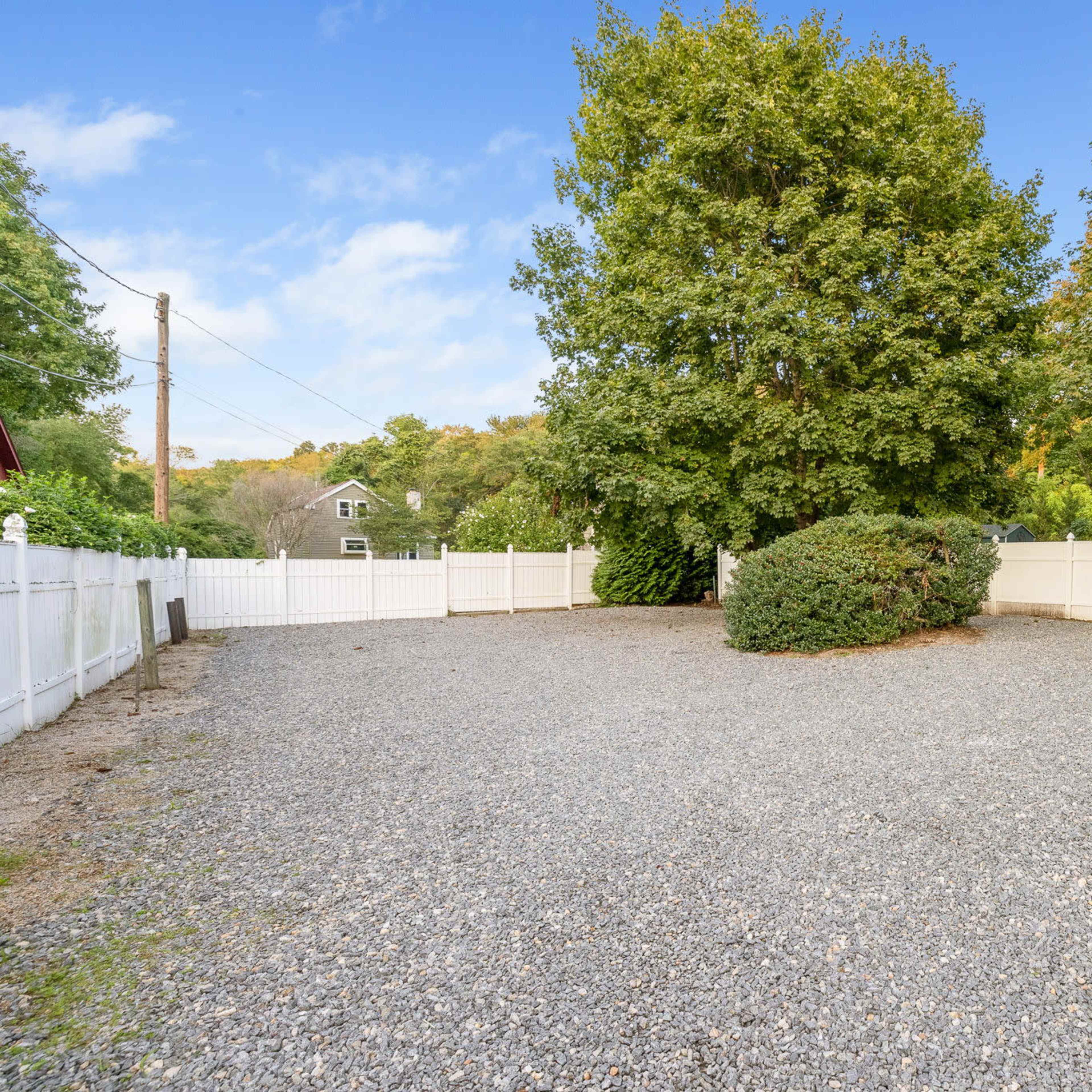 A gravel area is enclosed by a white fence and features two trees in the center.