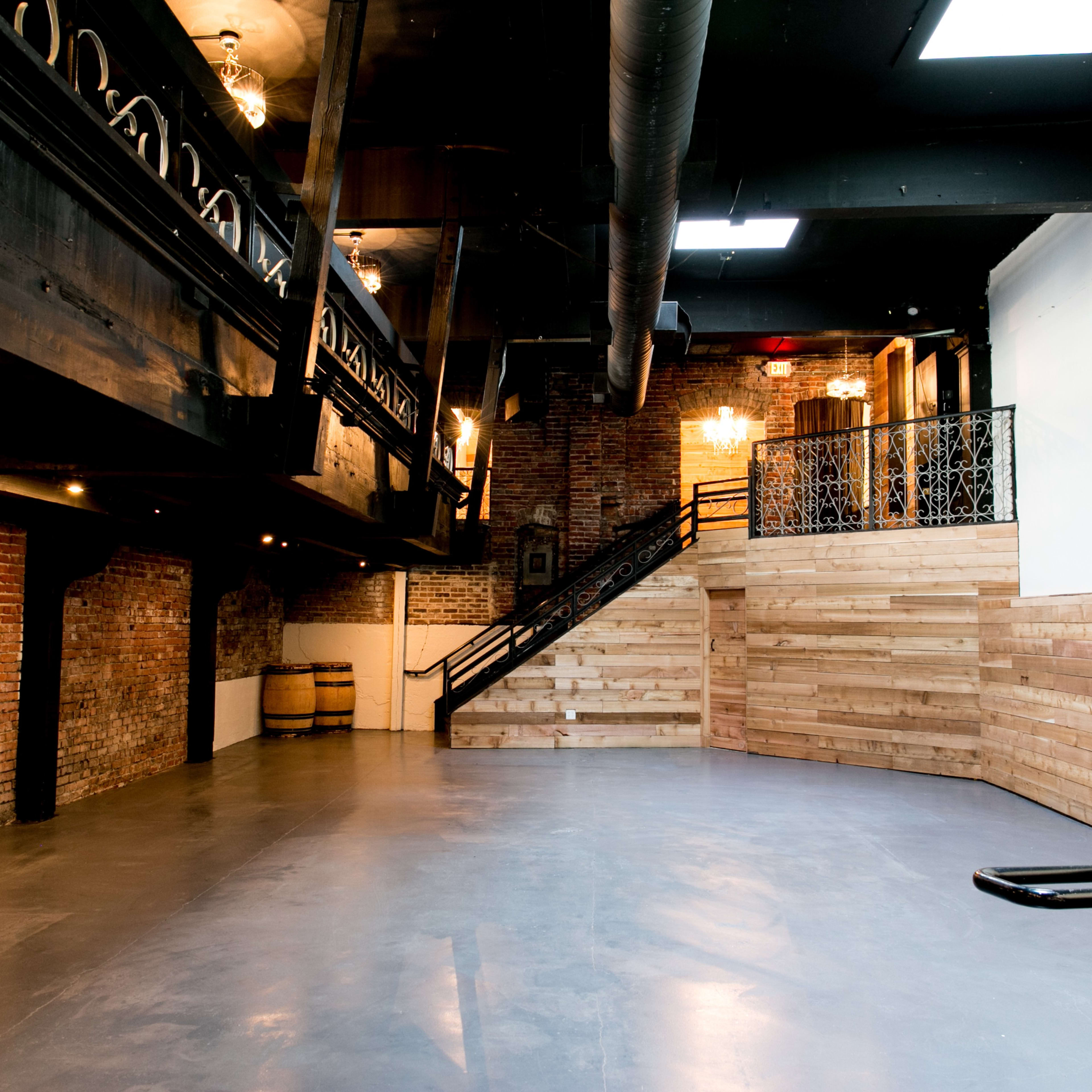 A spacious event venue with exposed brick walls, wooden features, and a staircase leading to an upper level.