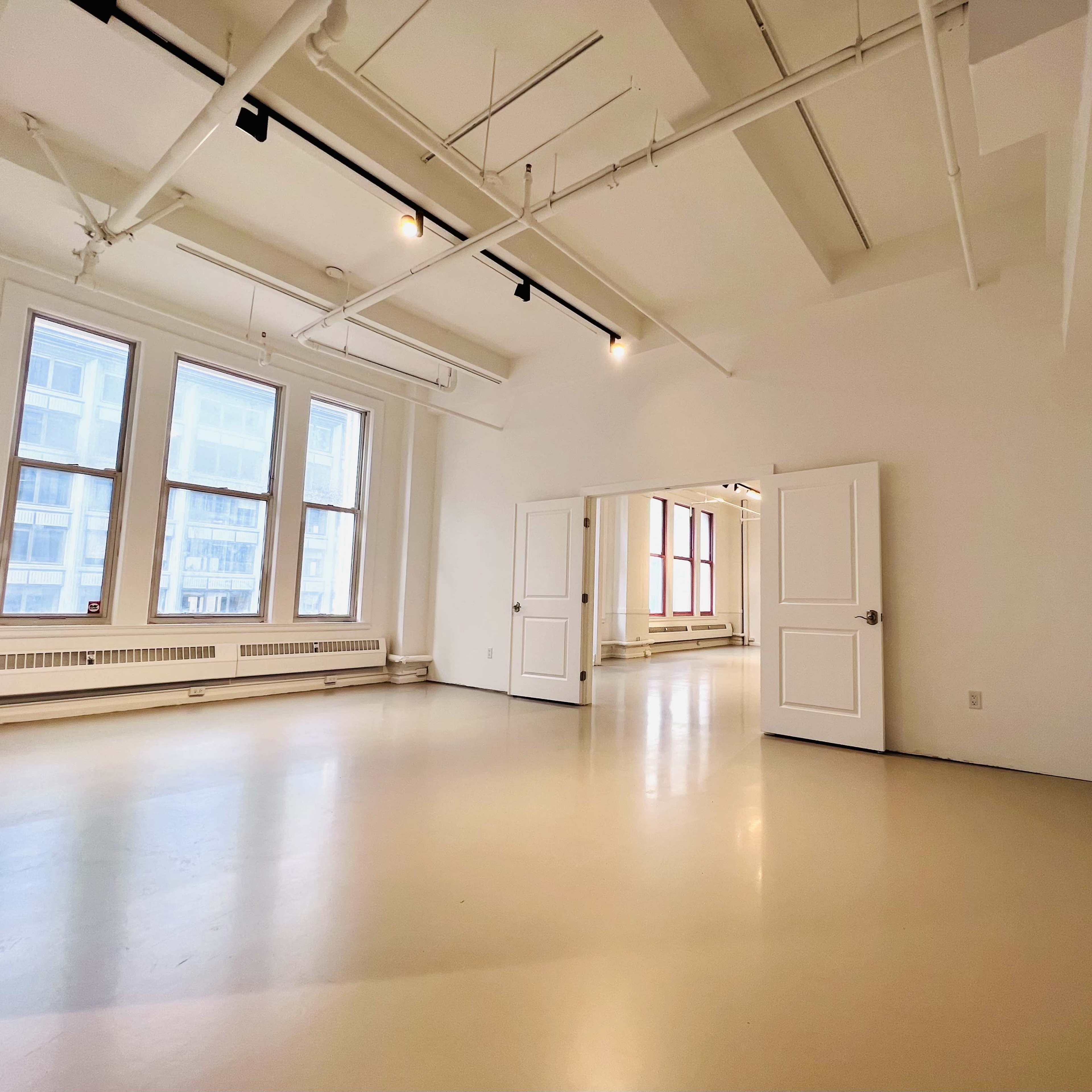 A spacious, empty room with large windows and two open doors leading to another room.