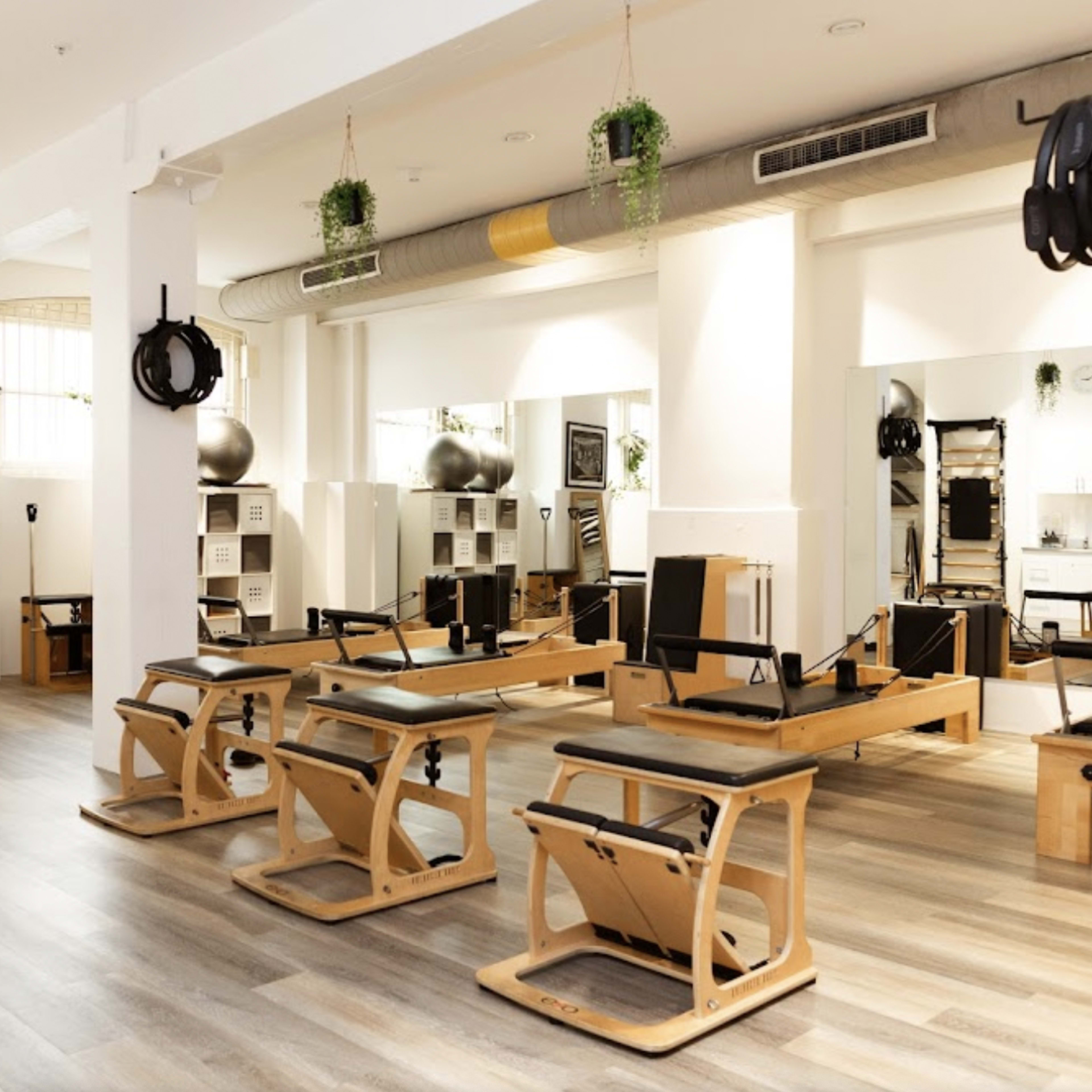 A modern Pilates studio with several Reformer machines arranged neatly along wooden flooring and large mirrors reflecting the space.