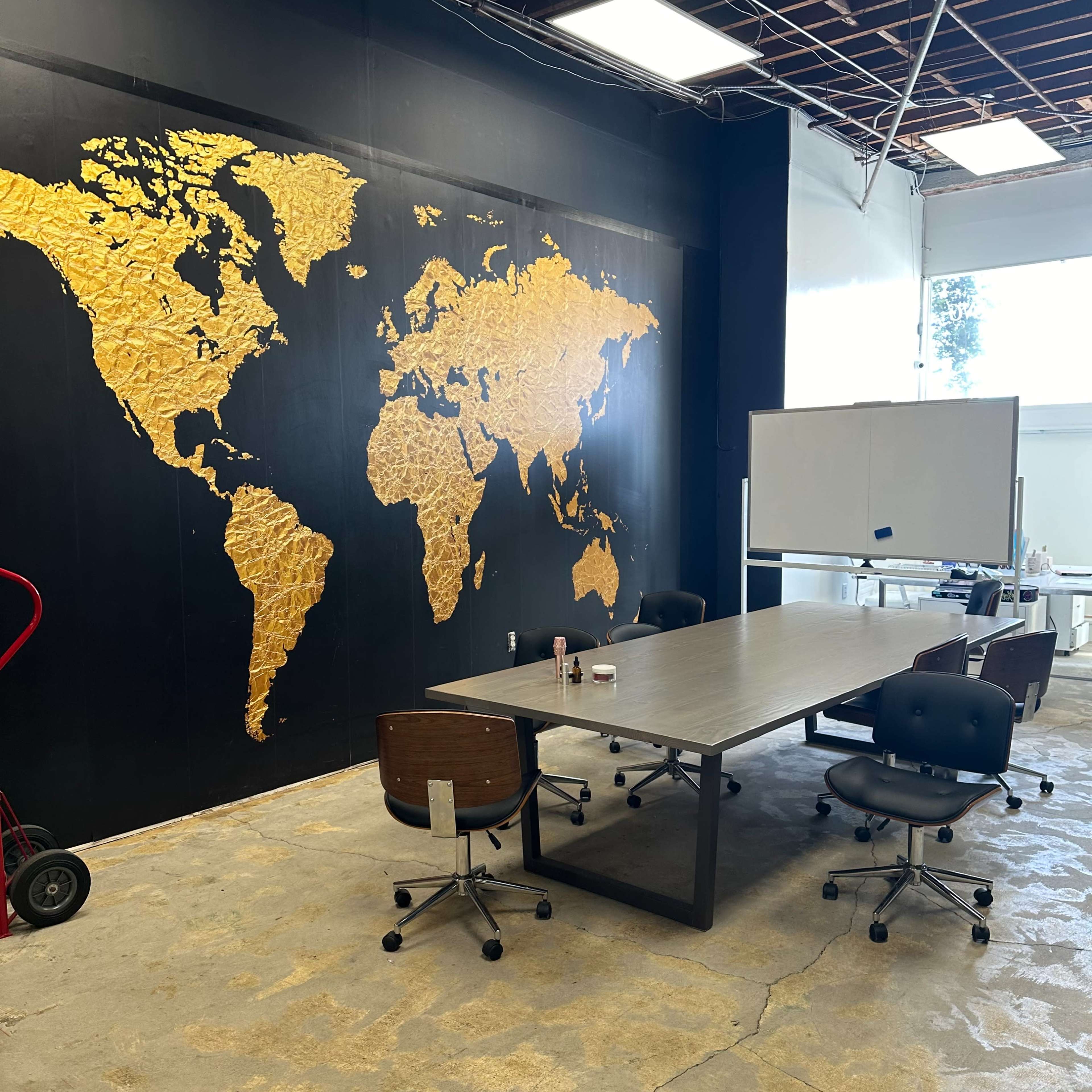 A meeting room with a large golden world map on a black wall, a central table, and several office chairs arranged around it.