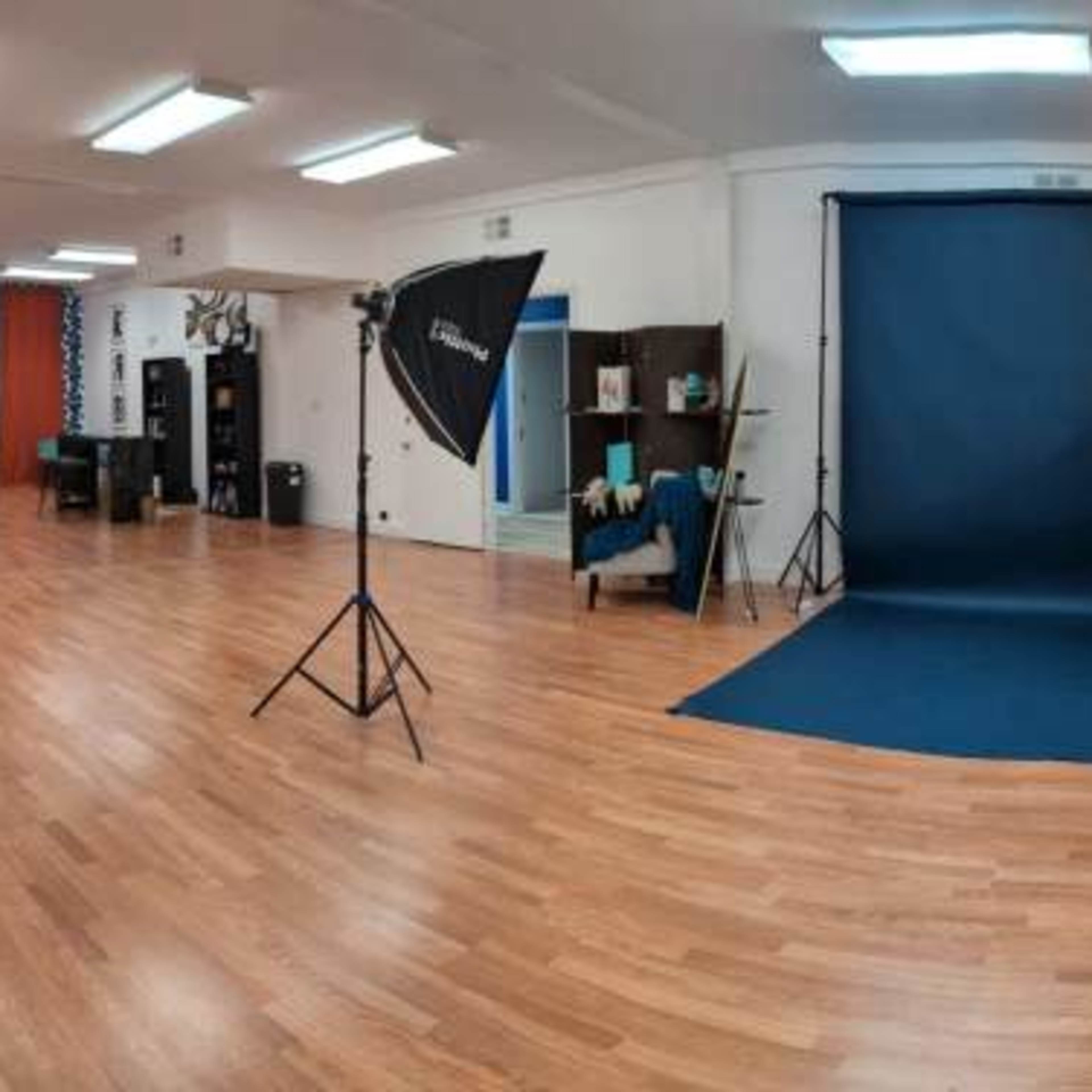 A spacious studio with multiple backdrops, lighting equipment, and a chair in the corner.