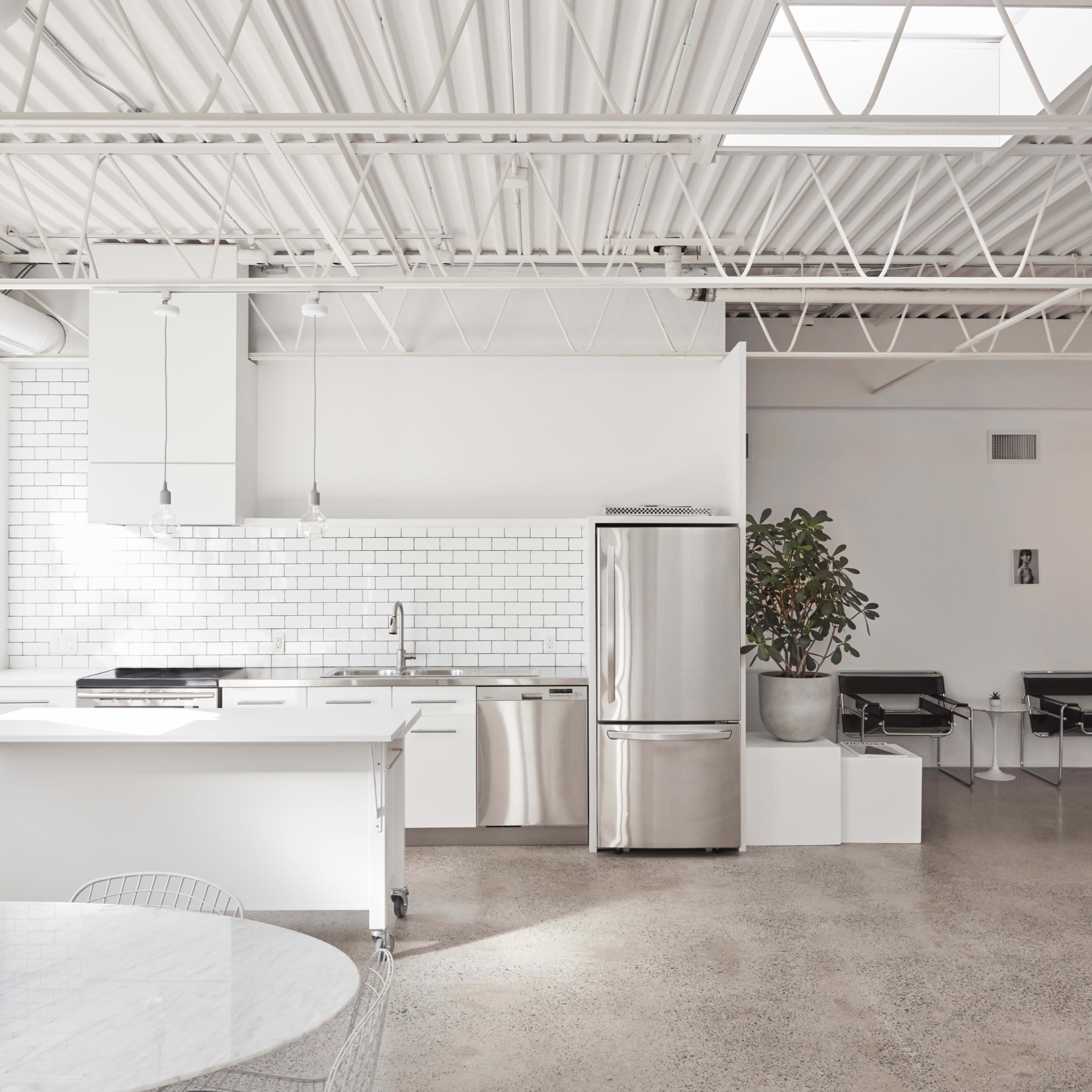 A modern, open-concept kitchen with stainless steel appliances, a white tile backsplash, and a concrete floor.