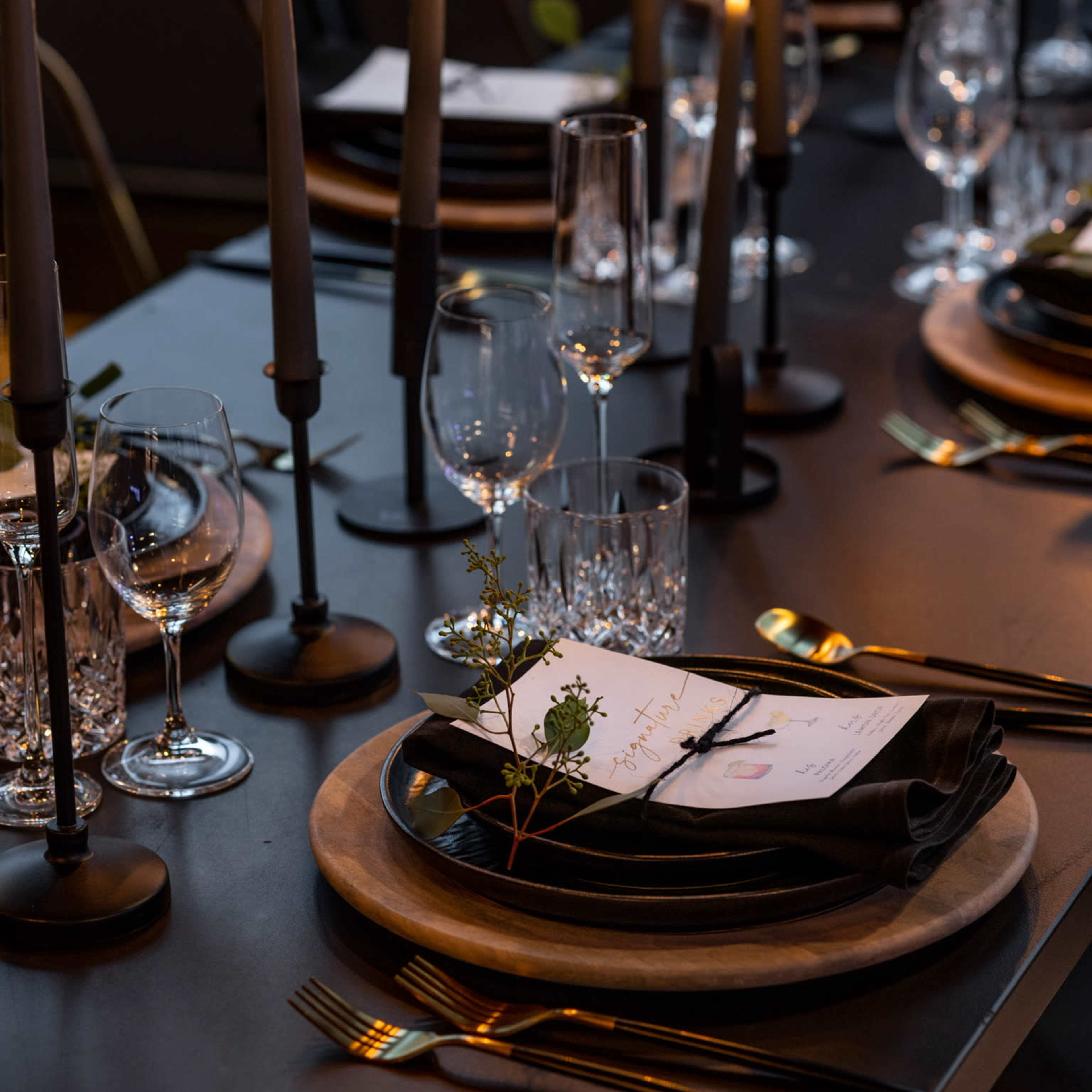 A elegantly set dining table features dark plates, crystal glassware, and tall candles, creating a formal atmosphere.