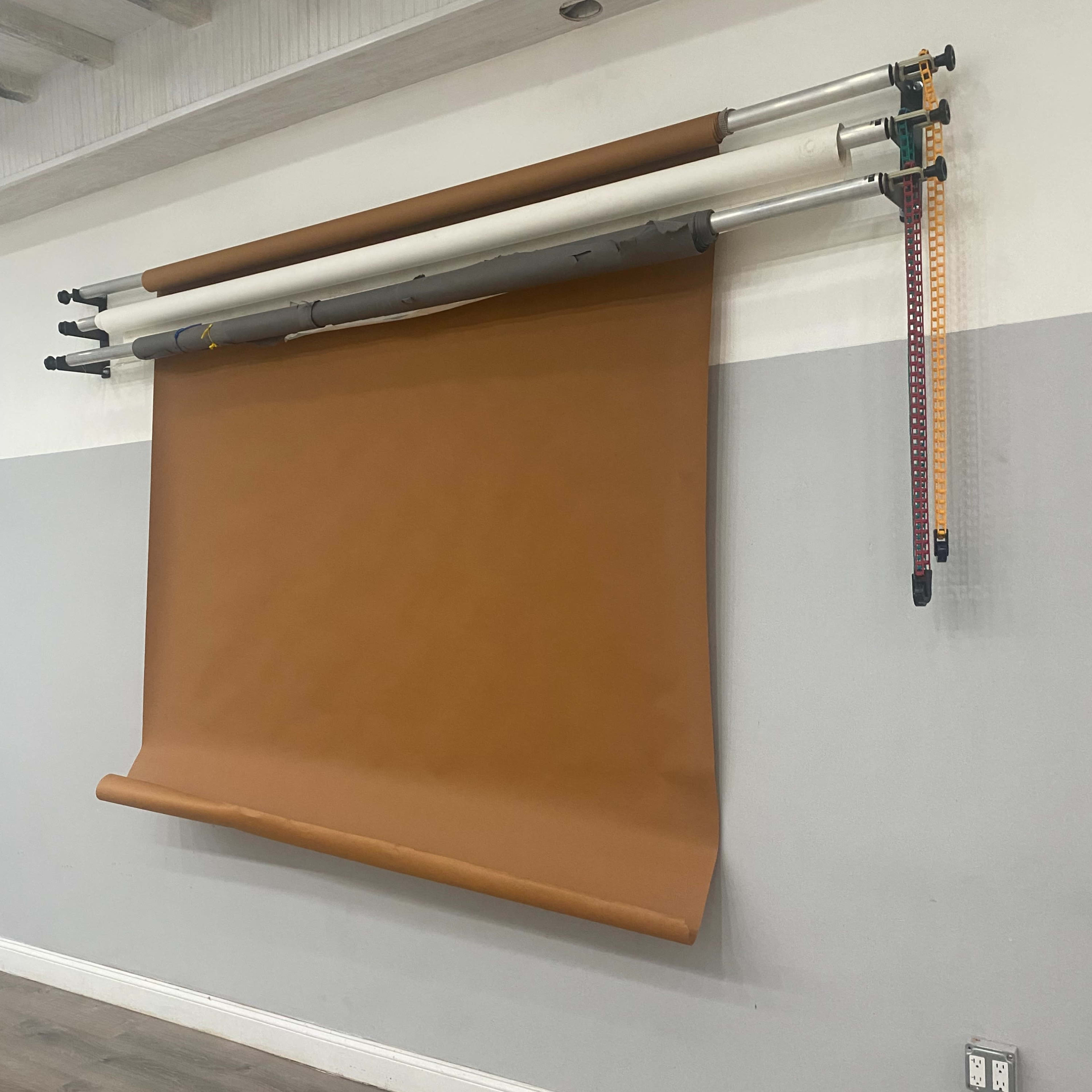 A large roll of brown backdrop paper is mounted on a wall, hanging from a set of poles above it.