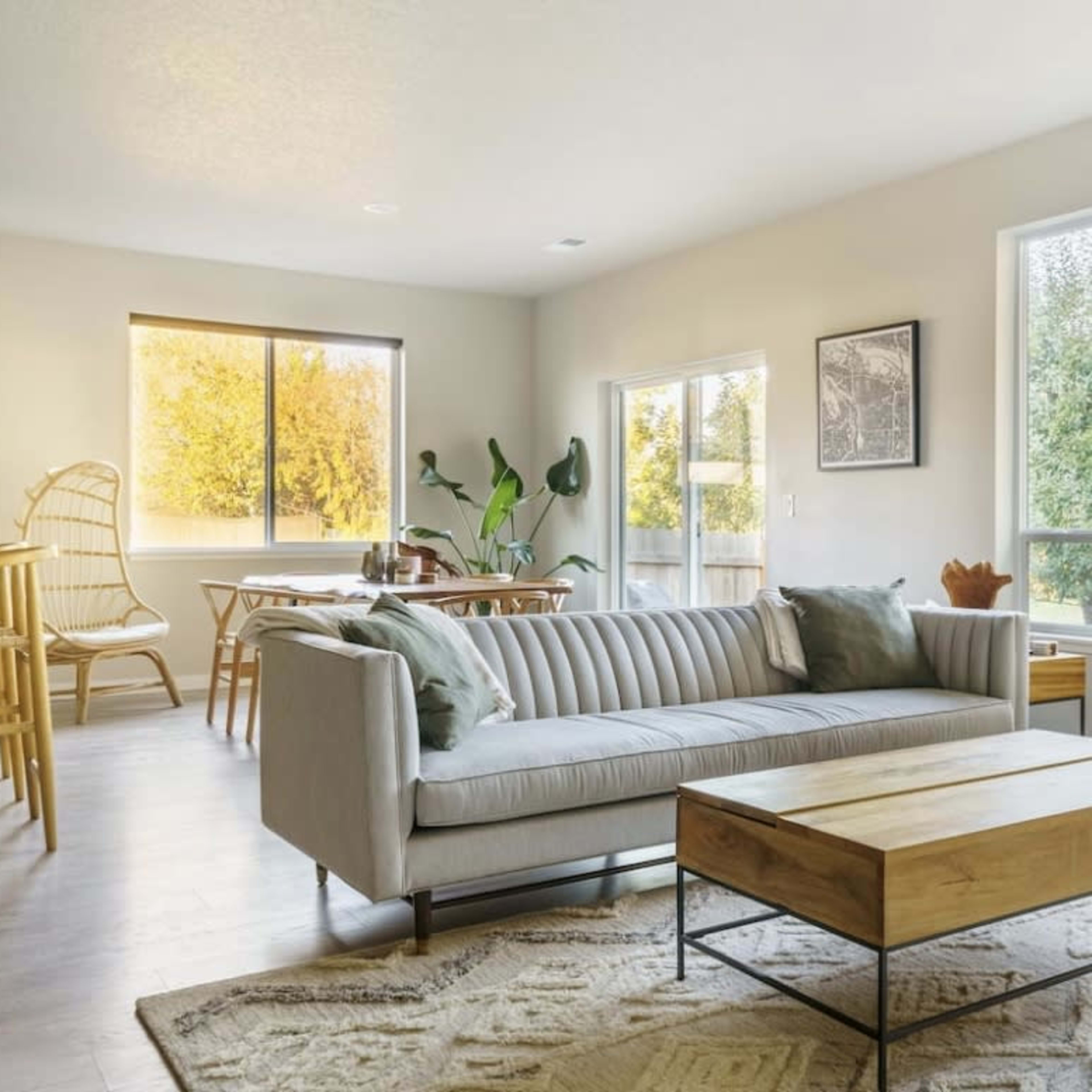 A modern living area features a striped sofa, a wooden coffee table, large windows, and a dining space connected to a kitchen.