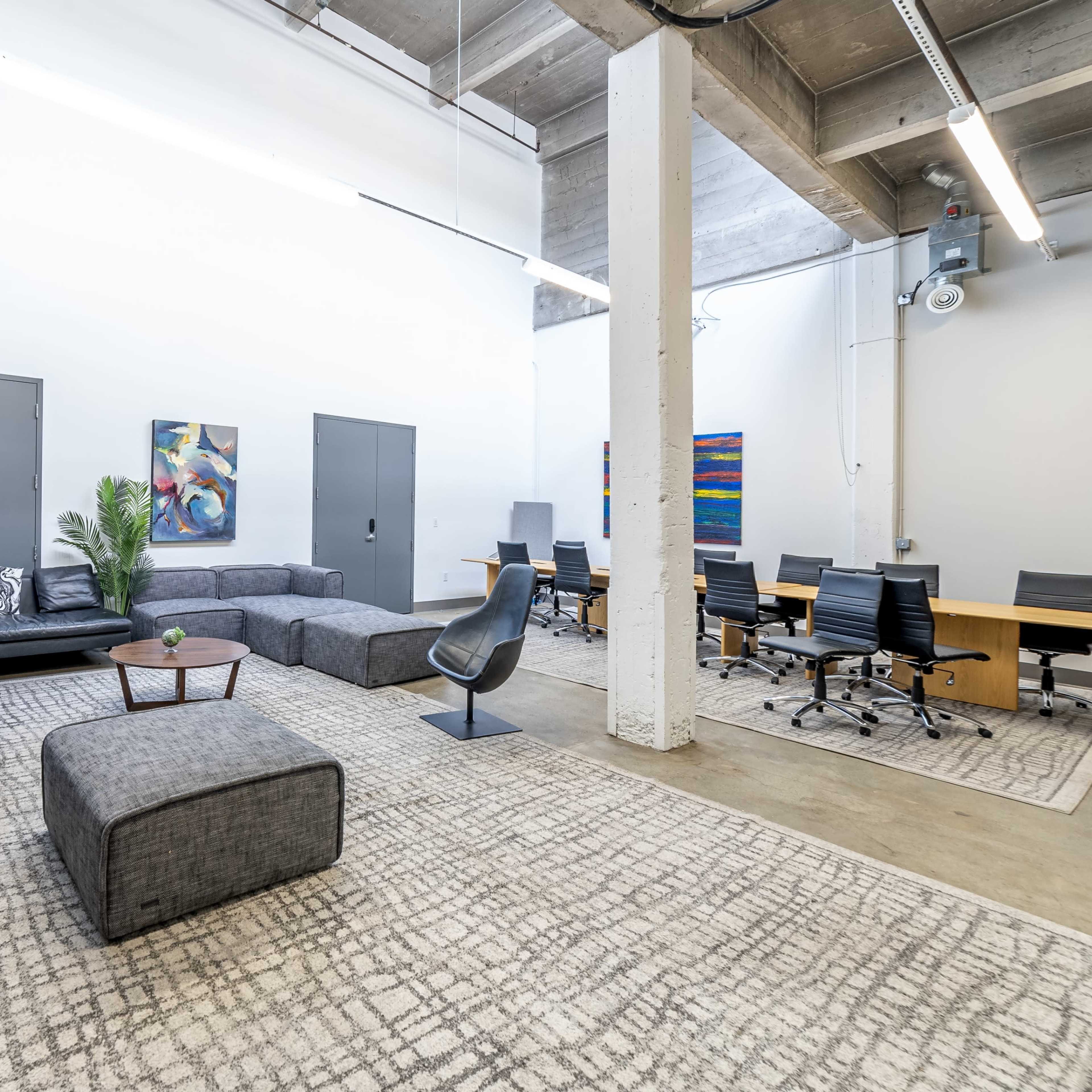 A modern office space featuring a casual seating area with a sectional sofa, a coffee table, and a meeting room with a long dining table and office chairs.
