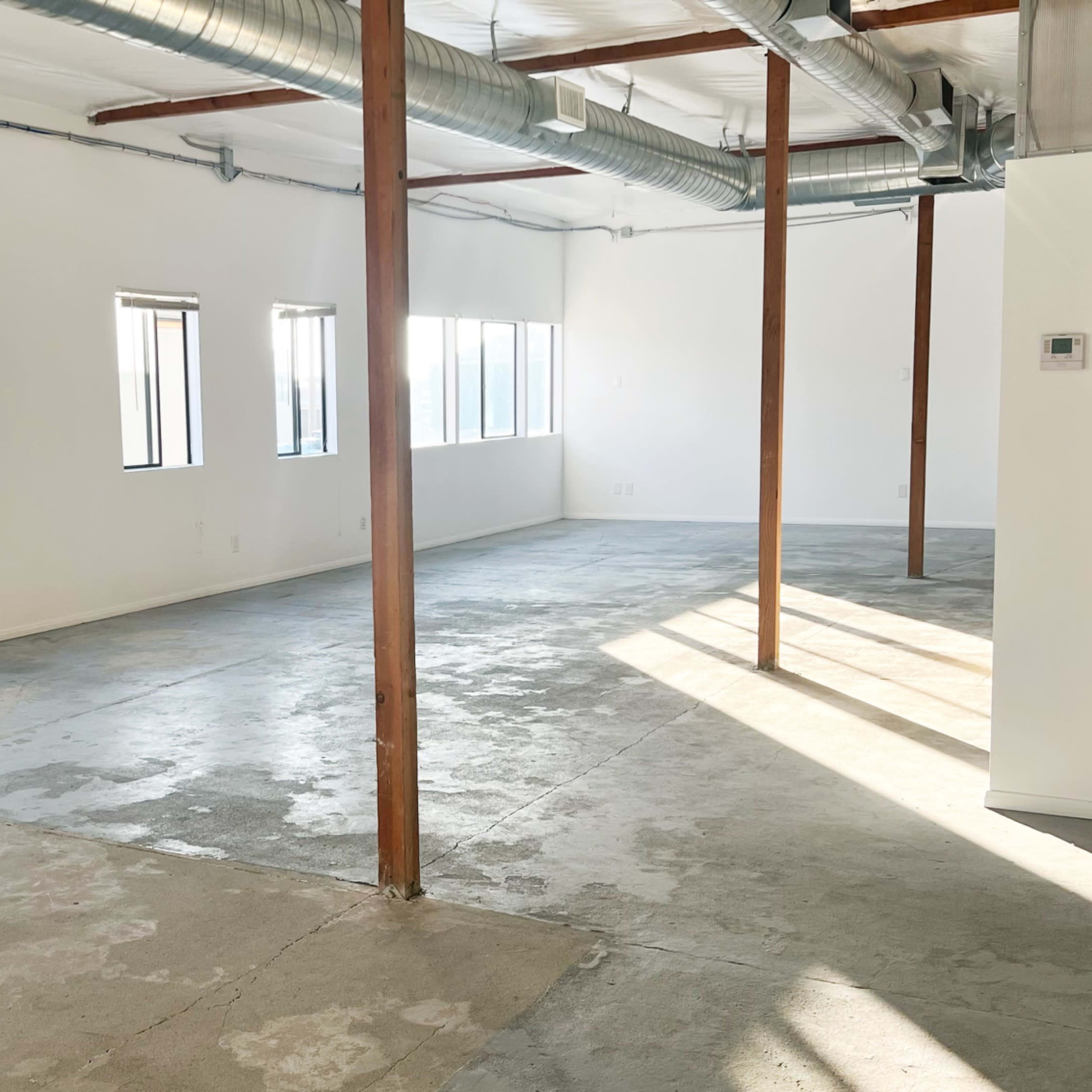 An empty room with concrete flooring, large windows, and exposed wooden beams.