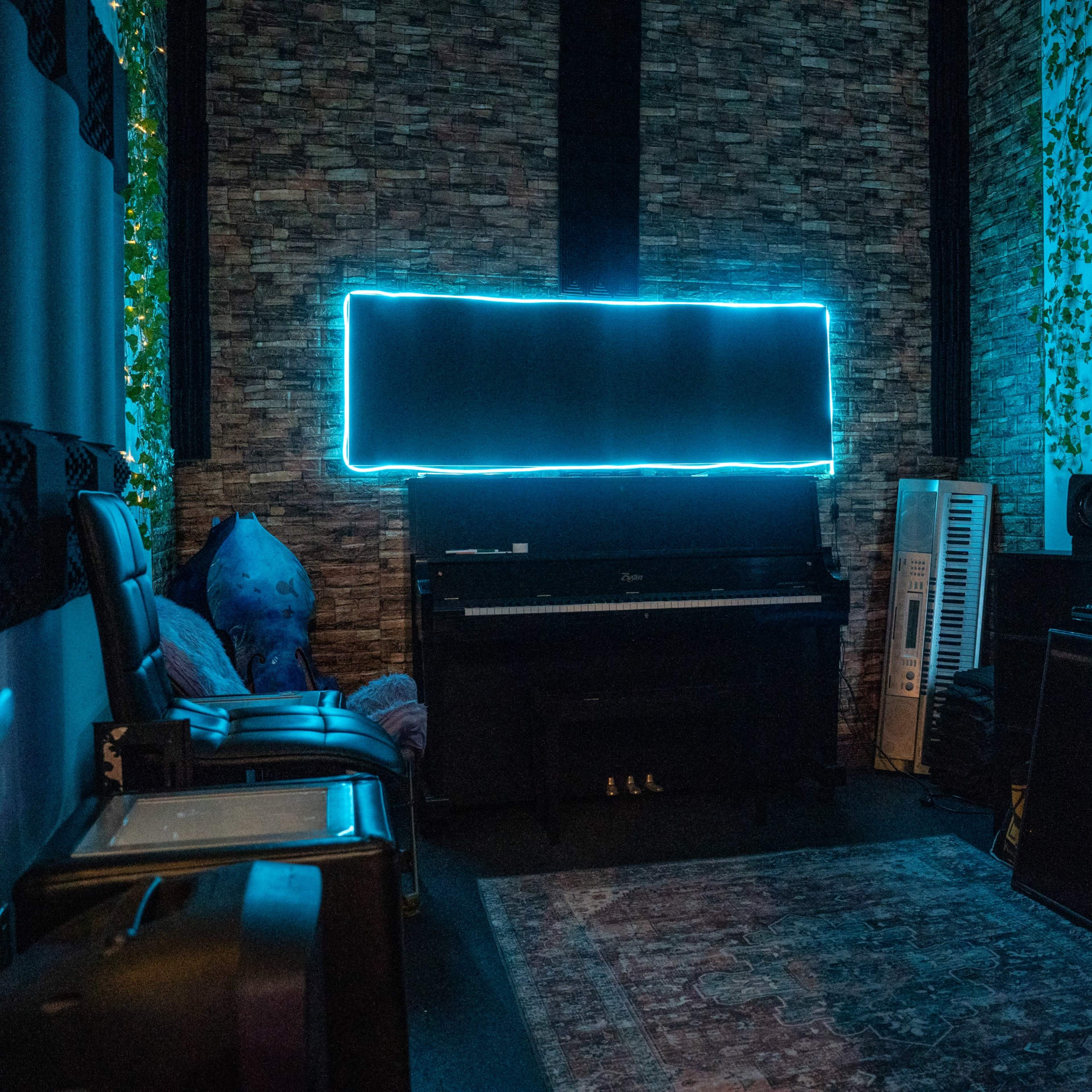 A recording studio with a piano, a keyboard, and various audio equipment, illuminated by neon blue lighting.