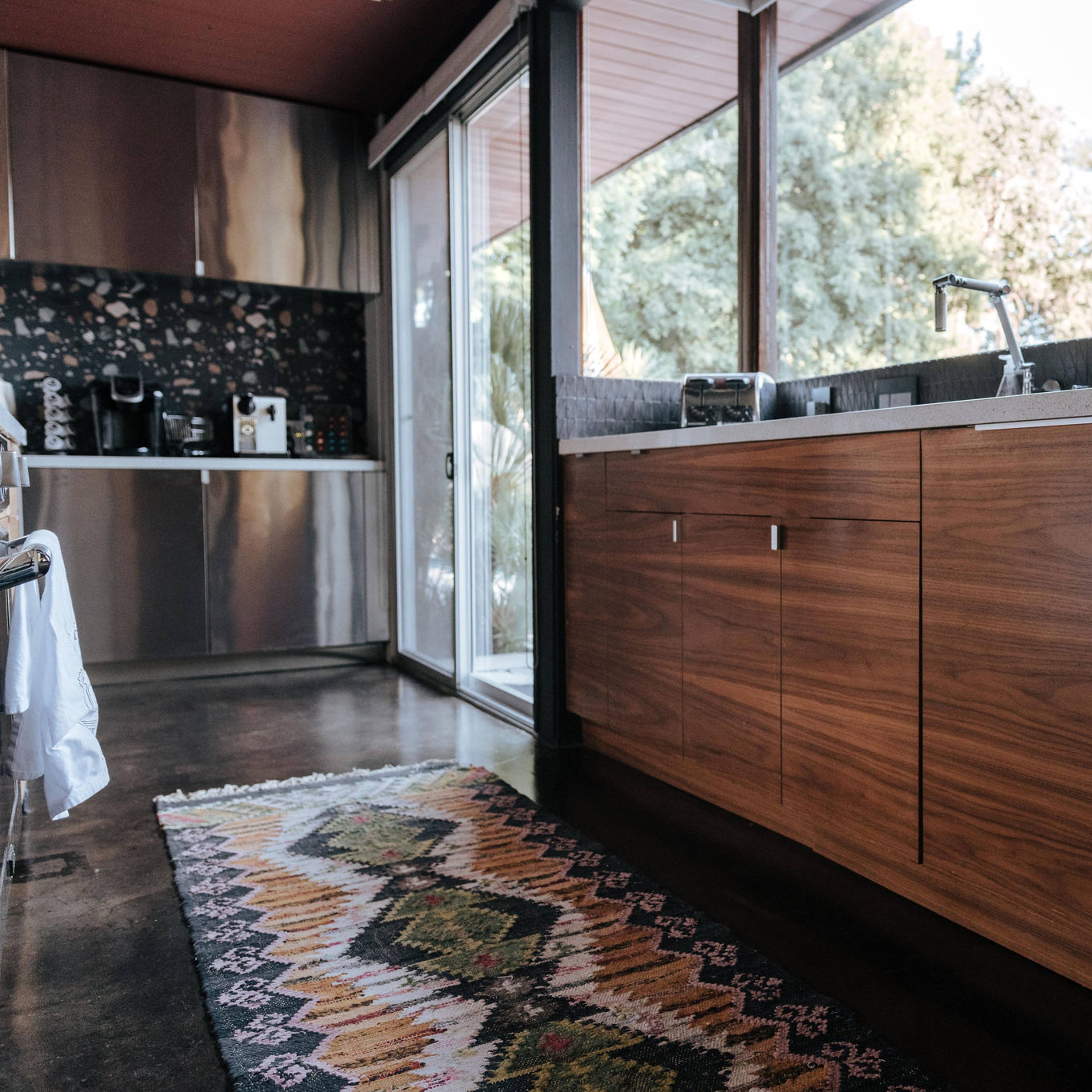 A modern kitchen with wooden cabinetry, a countertop, and a window view of greenery outside.