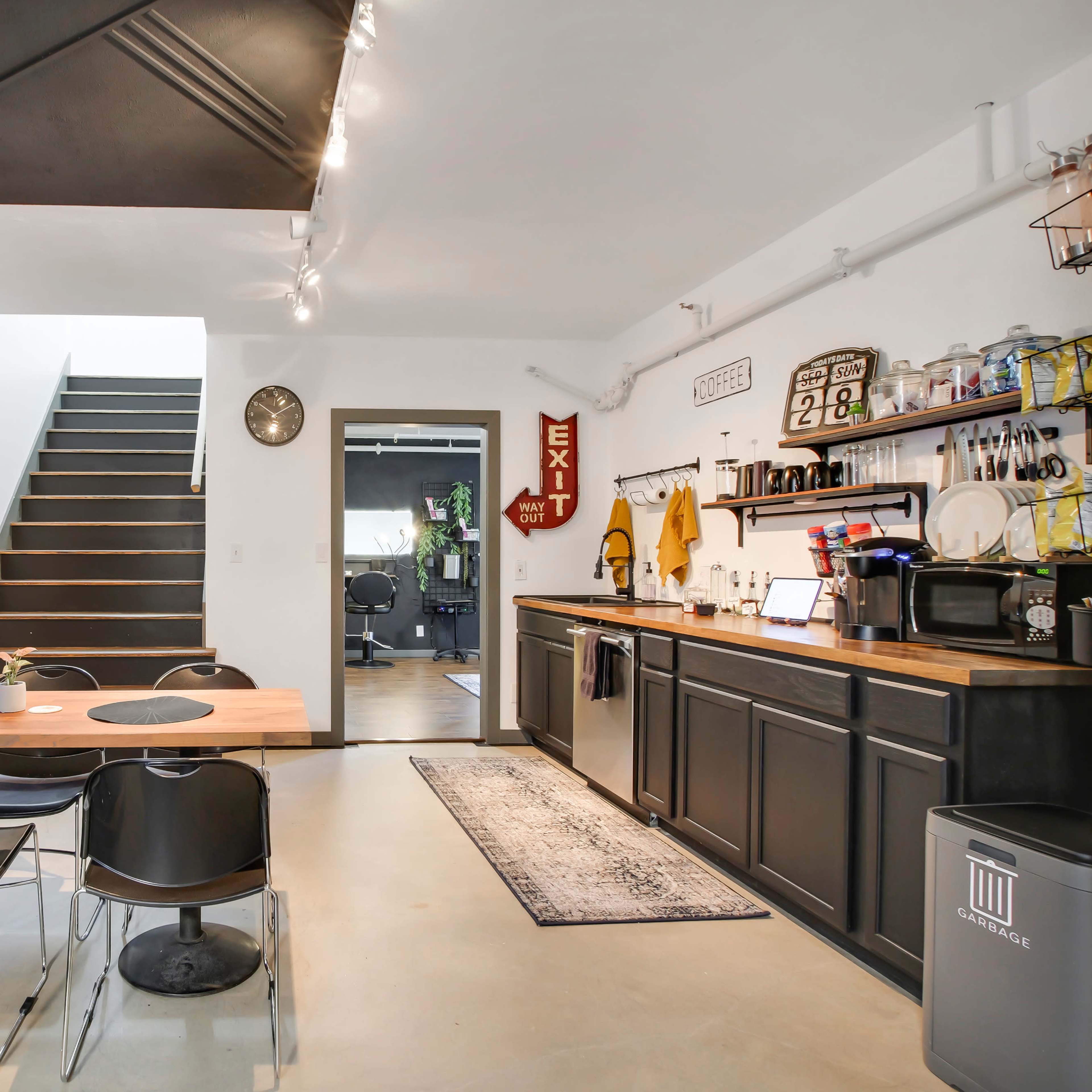 A modern kitchen and dining area with a wooden table, black chairs, and a staircase leading to an upper level.