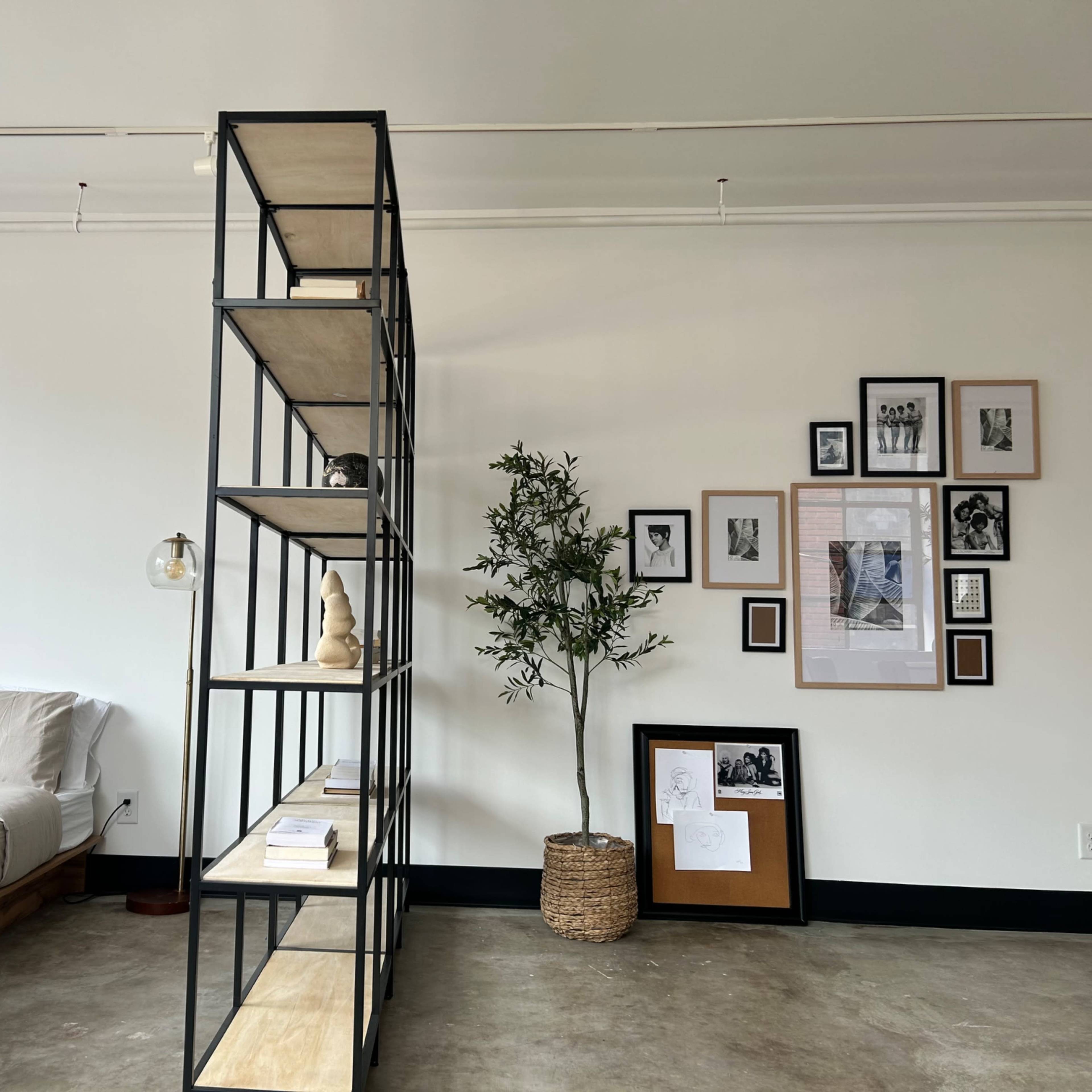 A modern bedroom with a bed on one side, a tall shelving unit in the center, and a collection of framed photos on the wall opposite the bed.