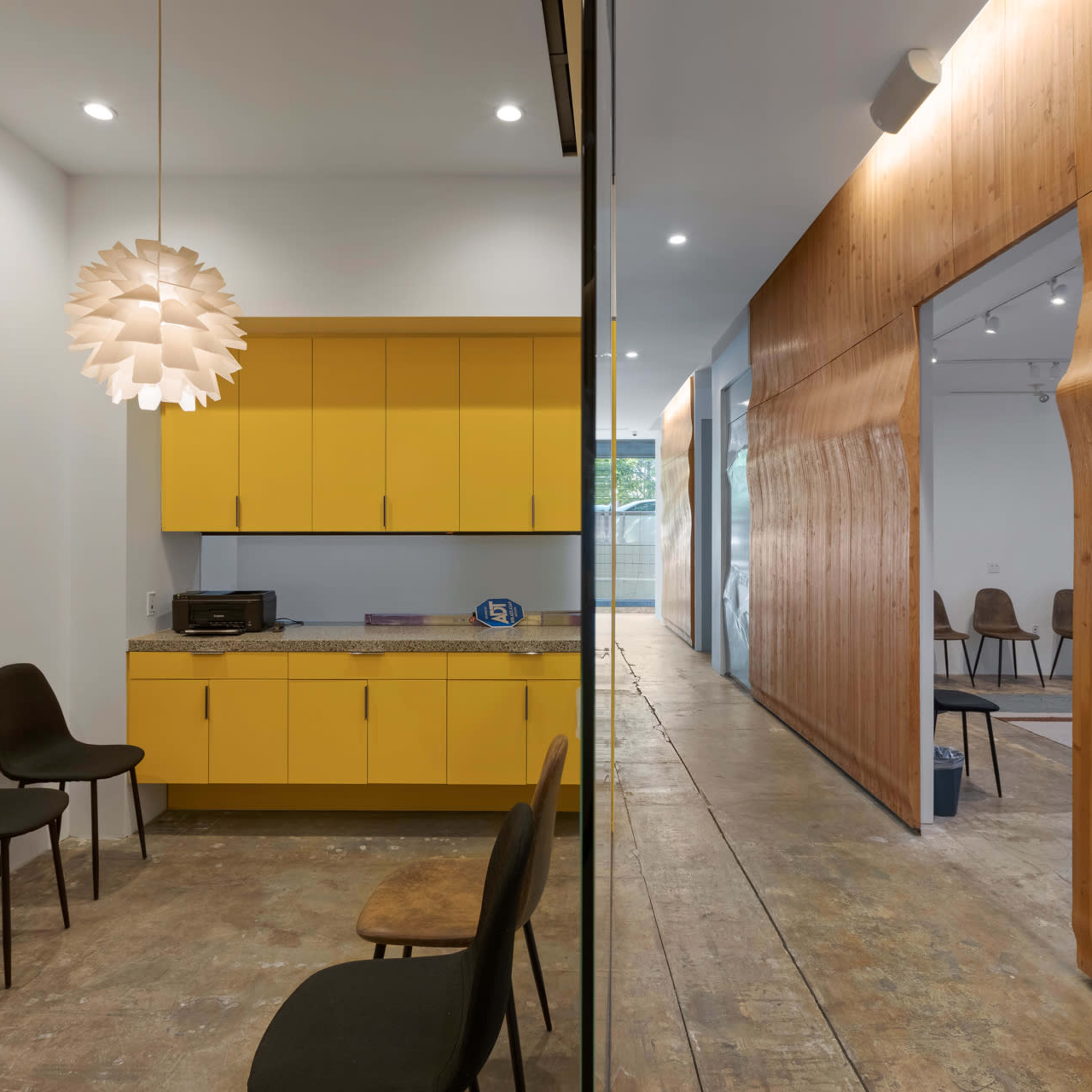 A modern room featuring a kitchen area with yellow cabinets, a seating space with black chairs, and a wooden wall that leads to another room.