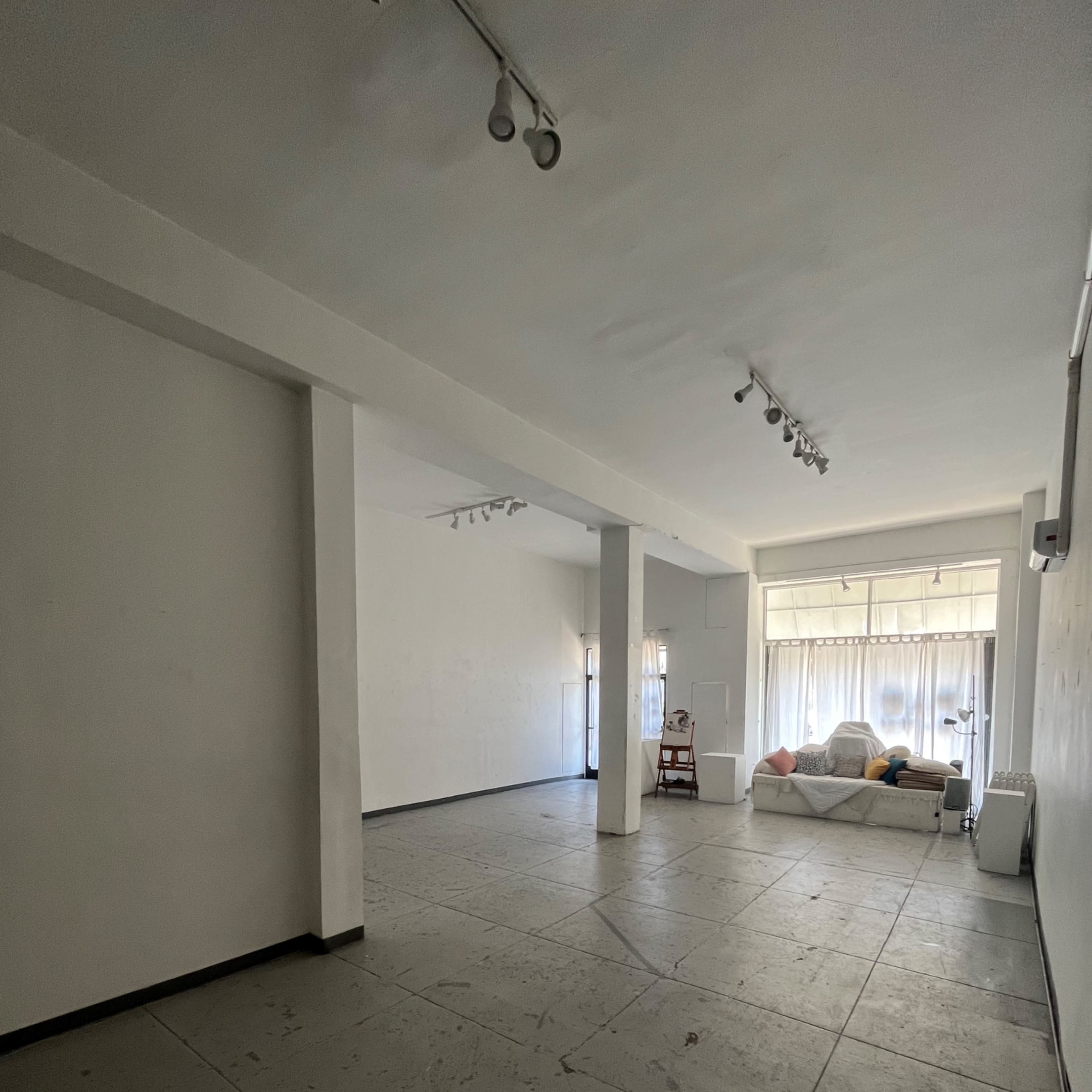 An empty, minimally furnished room with concrete flooring and large windows at one end.