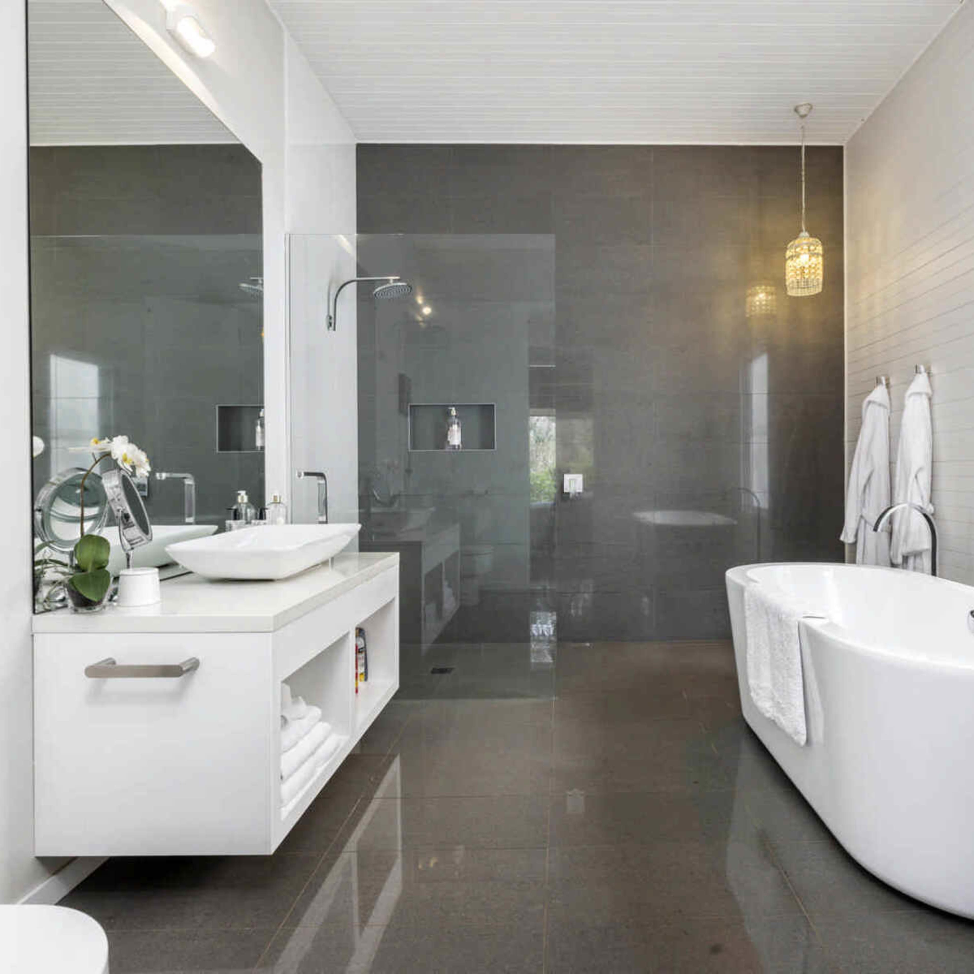 A modern bathroom featuring a freestanding bathtub, a wall-mounted sink with storage underneath, and a large mirror, all set against a dark accent wall.