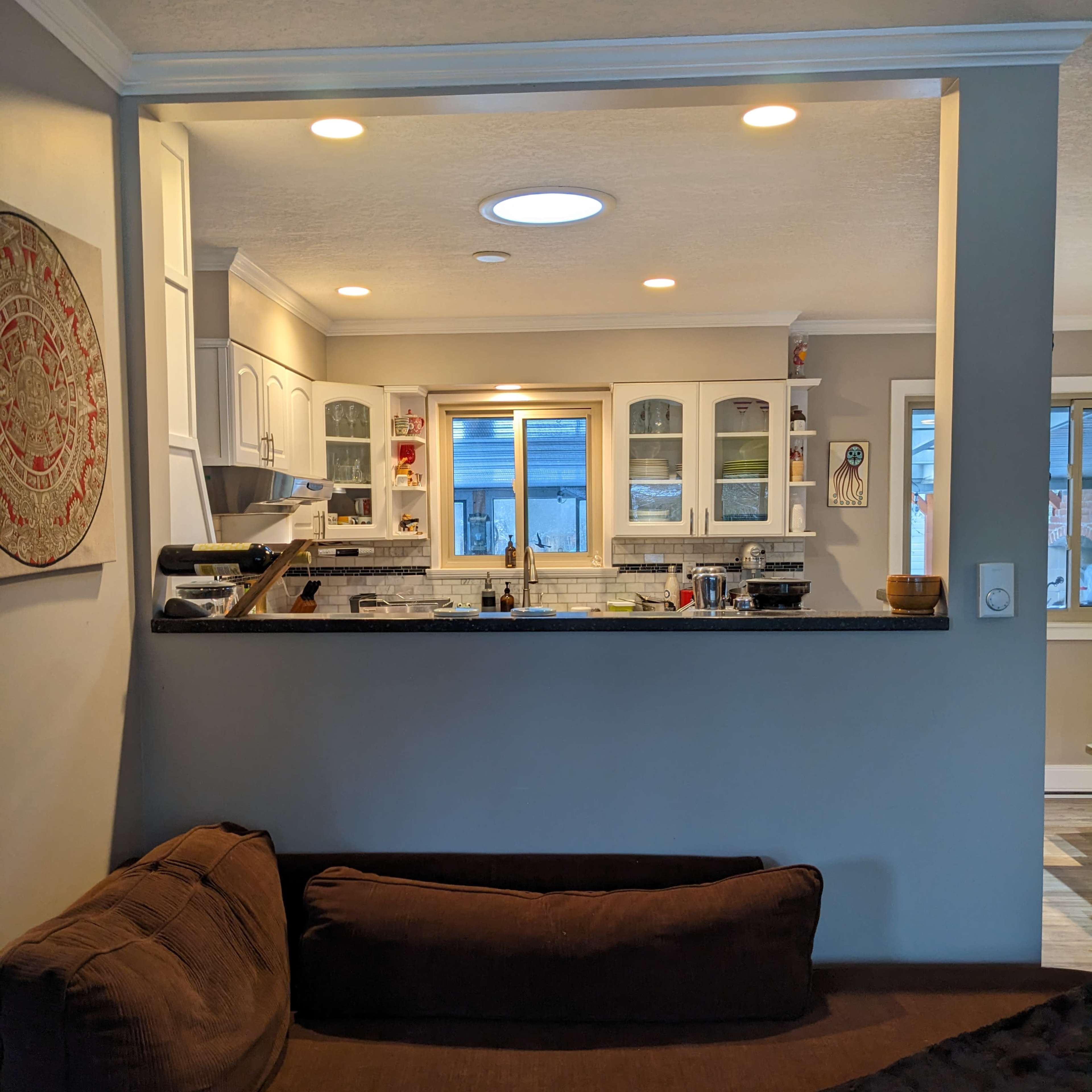 A cozy living space with a brown couch facing an open kitchen that features white cabinets and a countertop.