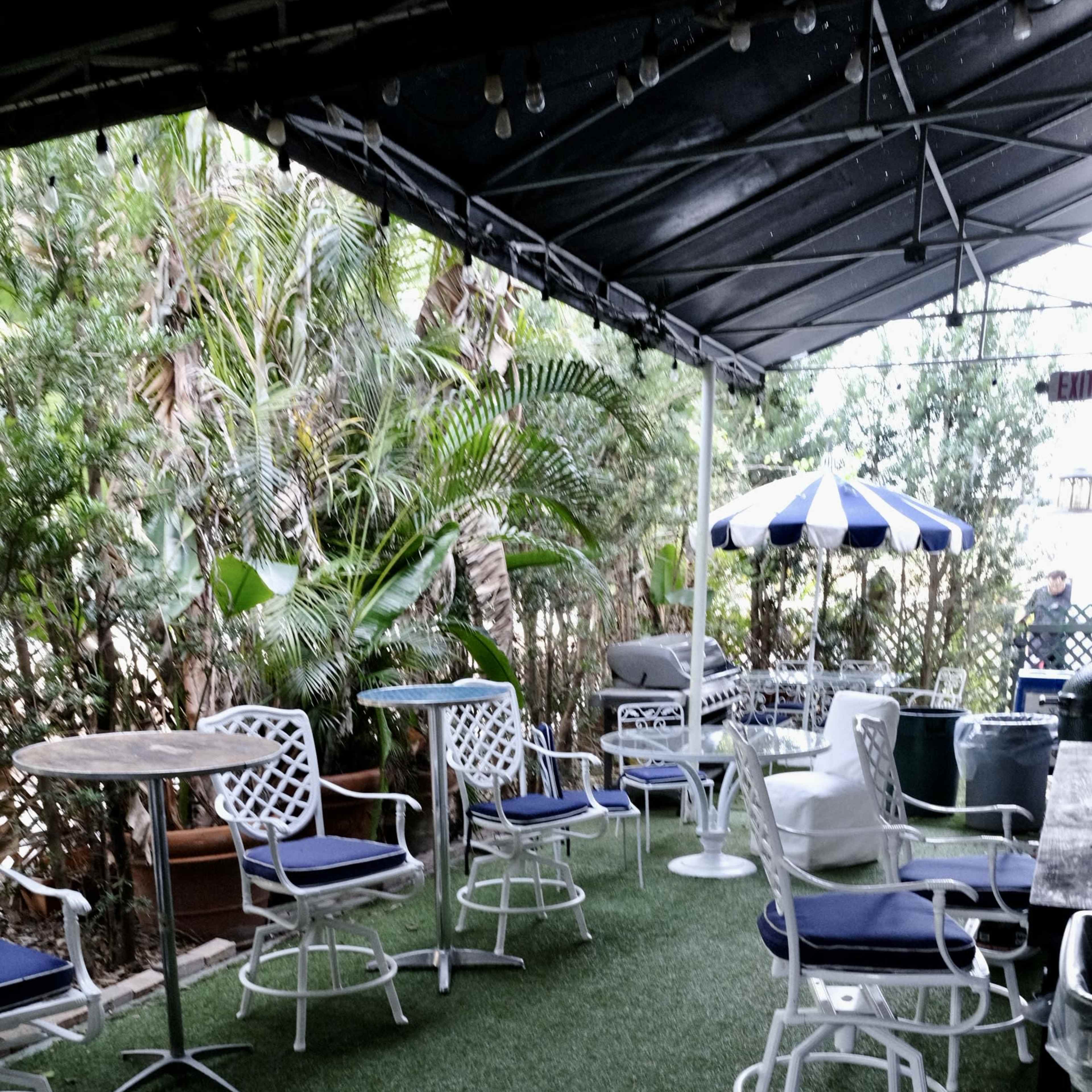 An outdoor patio with white metal furniture, including tables and chairs, set on artificial grass surrounded by greenery.
