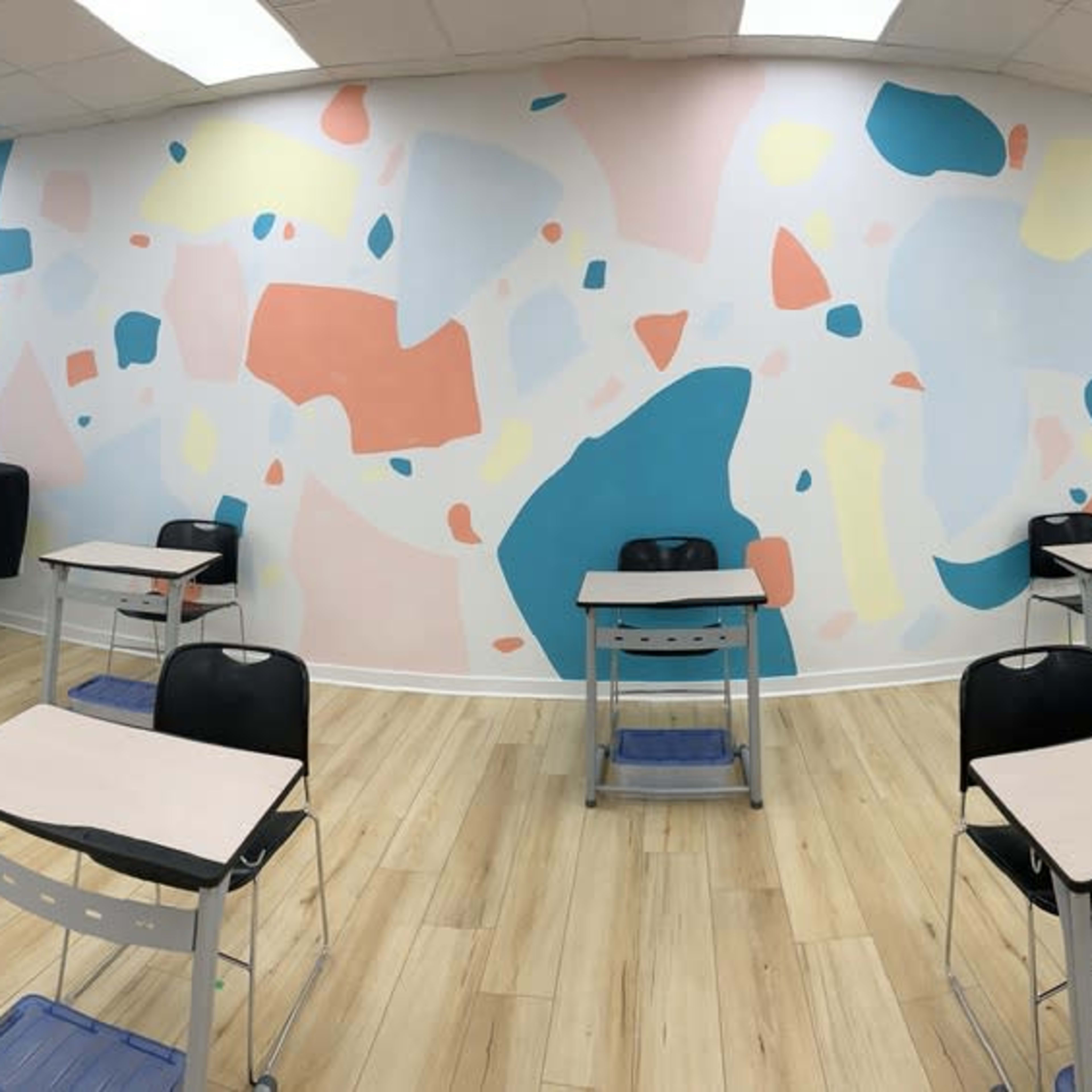 A modern classroom with several black chairs and desks arranged in a circular layout, featuring a colorful abstract mural on the walls.