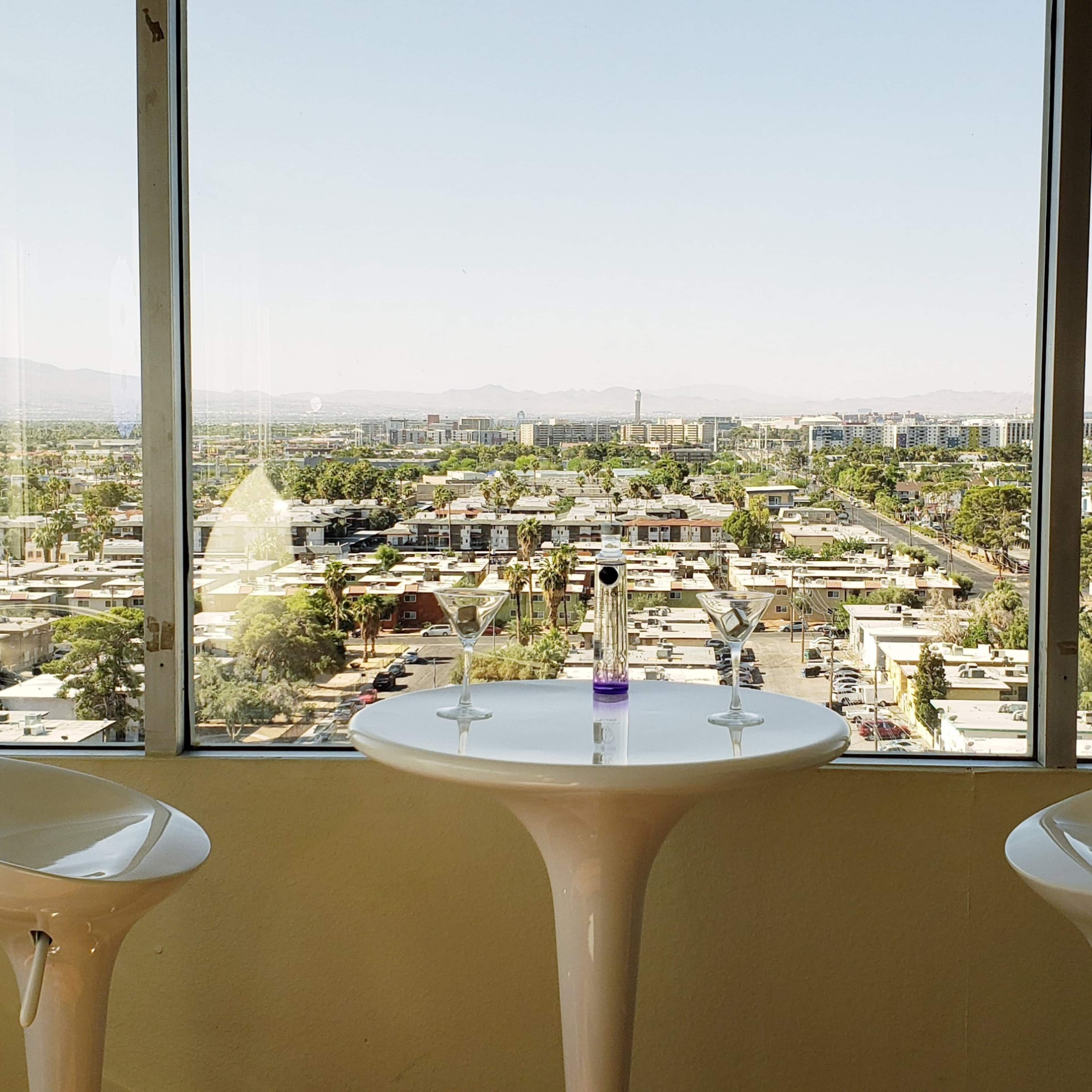 A bright room with two white chairs and a small round table, overlooking a sprawling urban landscape through large windows.