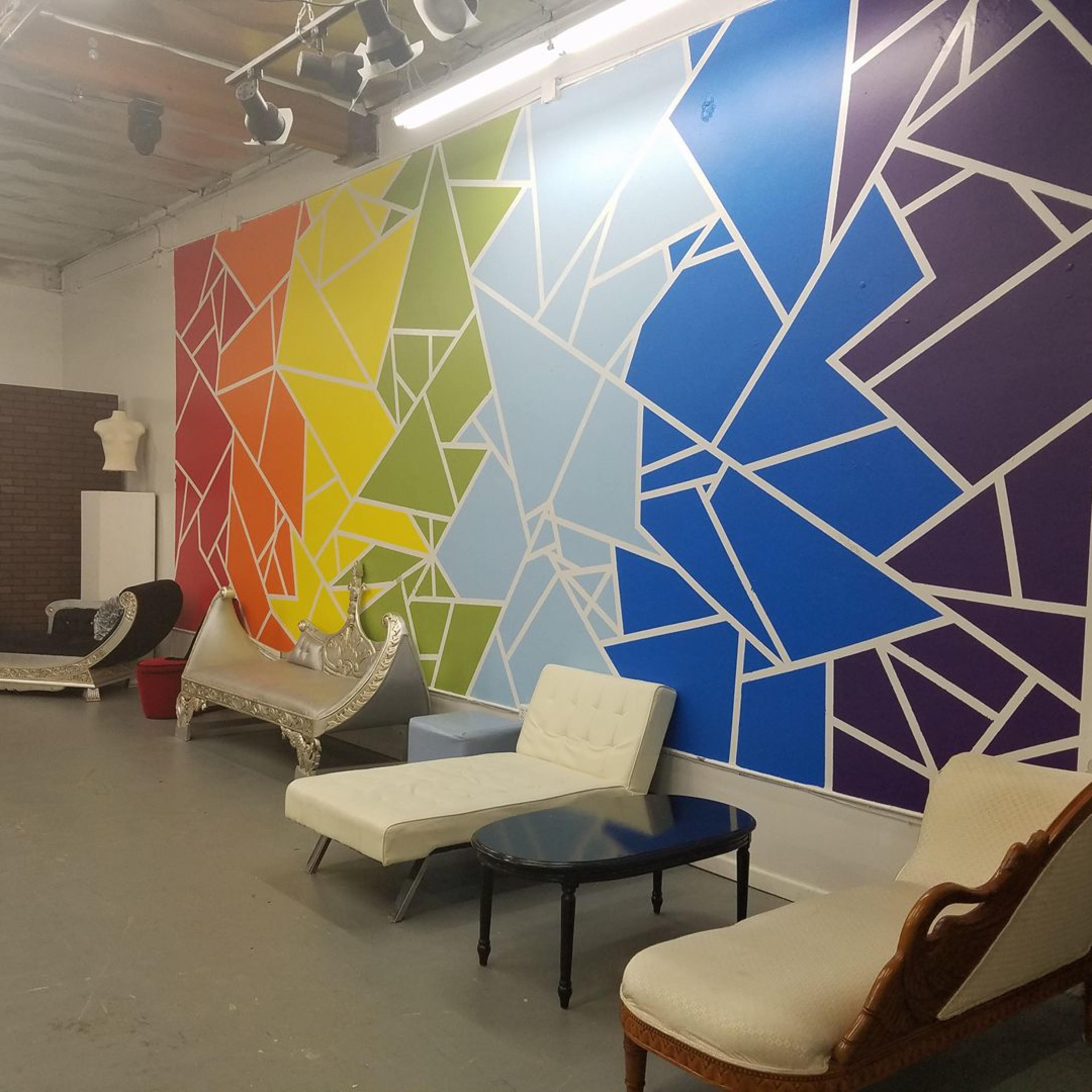 A spacious room with a colorful geometric mural on one wall and various couches arranged along the floor.