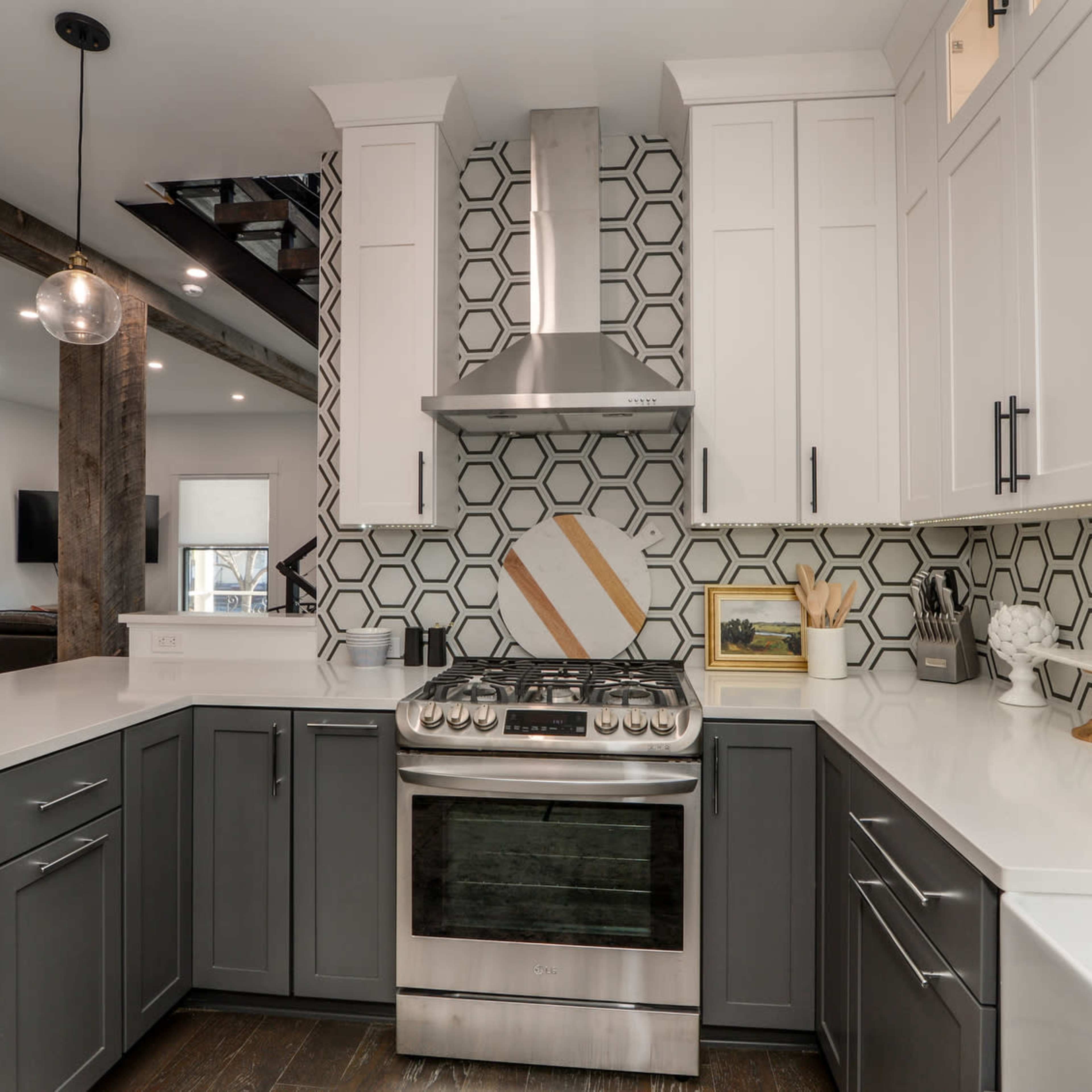 A modern kitchen features gray and white cabinetry, a stainless steel stove, and a geometric tile backsplash.